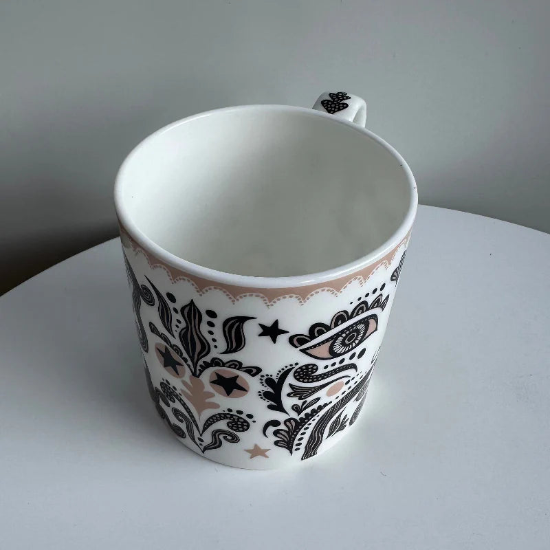 White mug with black and brown floral pattern on a white surface