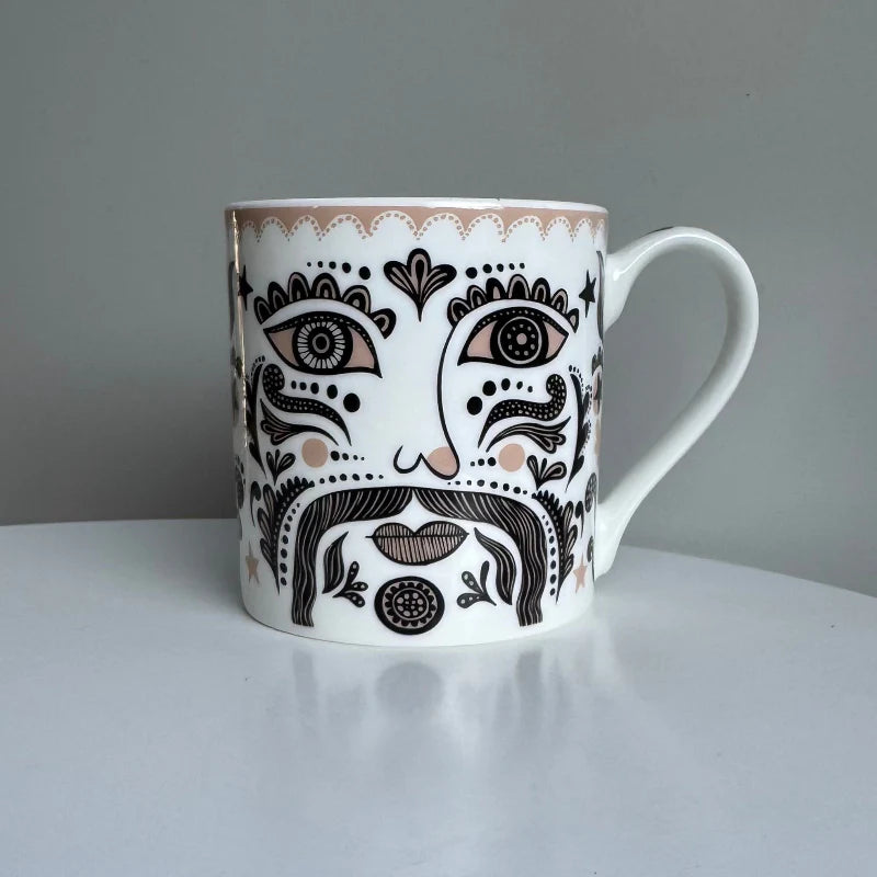 White mug with black and brown decorative design on a white surface with a light gray background