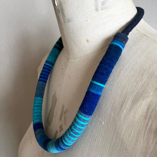 Striped fabric necklace in shades of blue and teal, displayed on a mannequin.