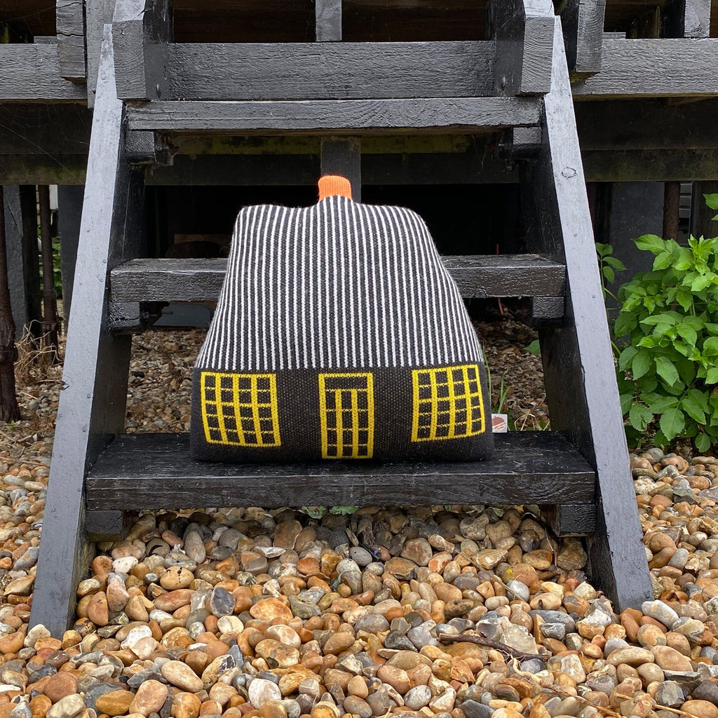 A striped black and white cushion with yellow windows and an orange handle by Donna Wilson on wooden stairs.