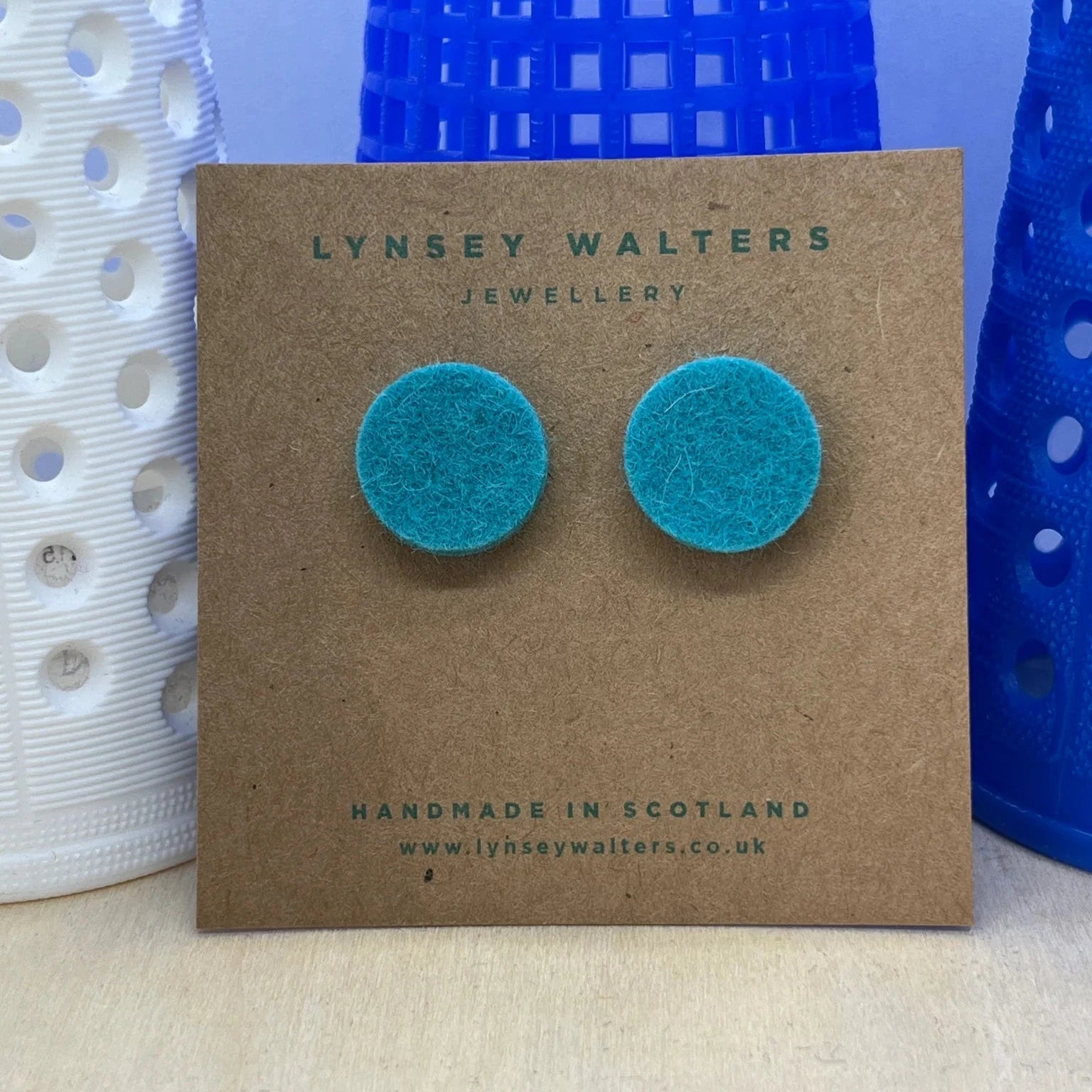 Pair of teal felt circle stud earrings displayed on a brown card.  Handmade in Scotland.
