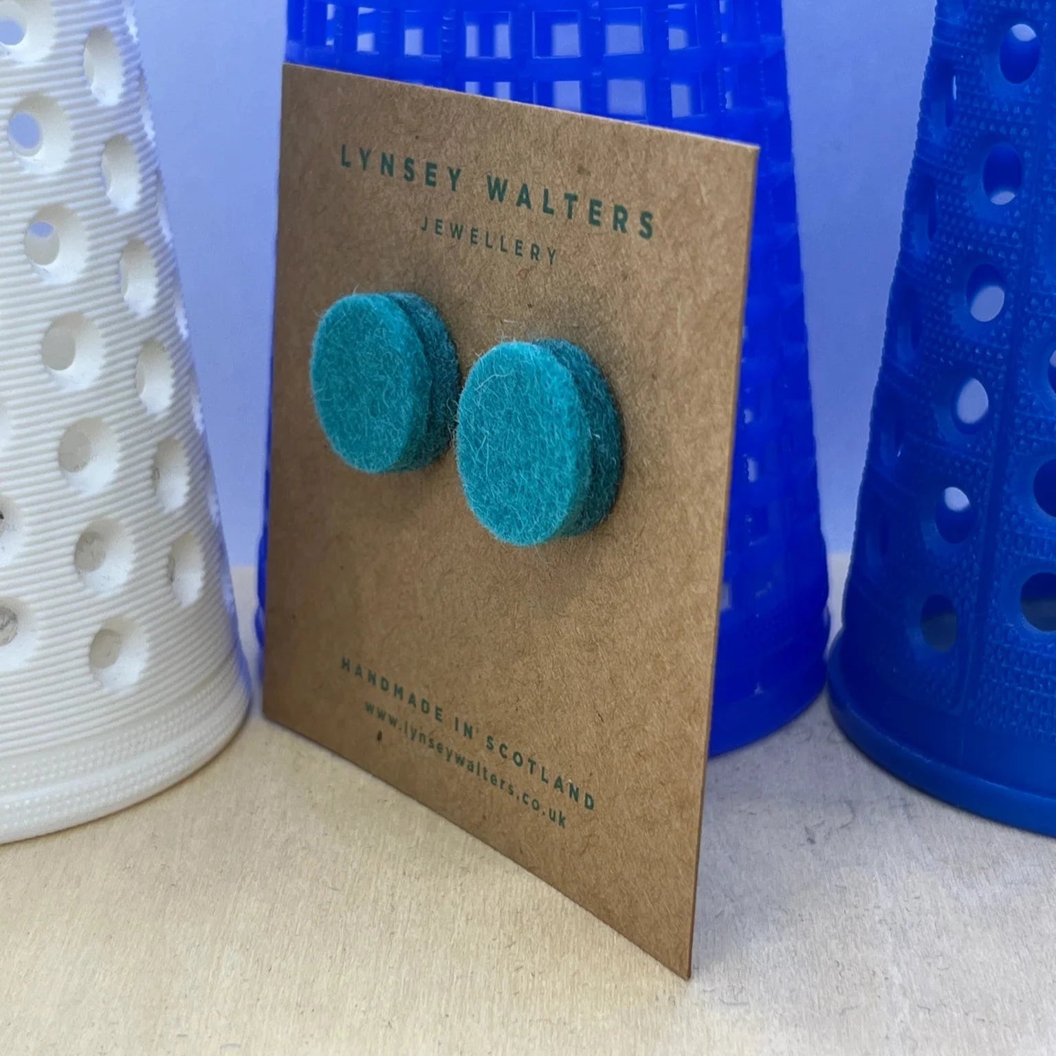 Pair of teal felt stud earrings displayed on a brown card.