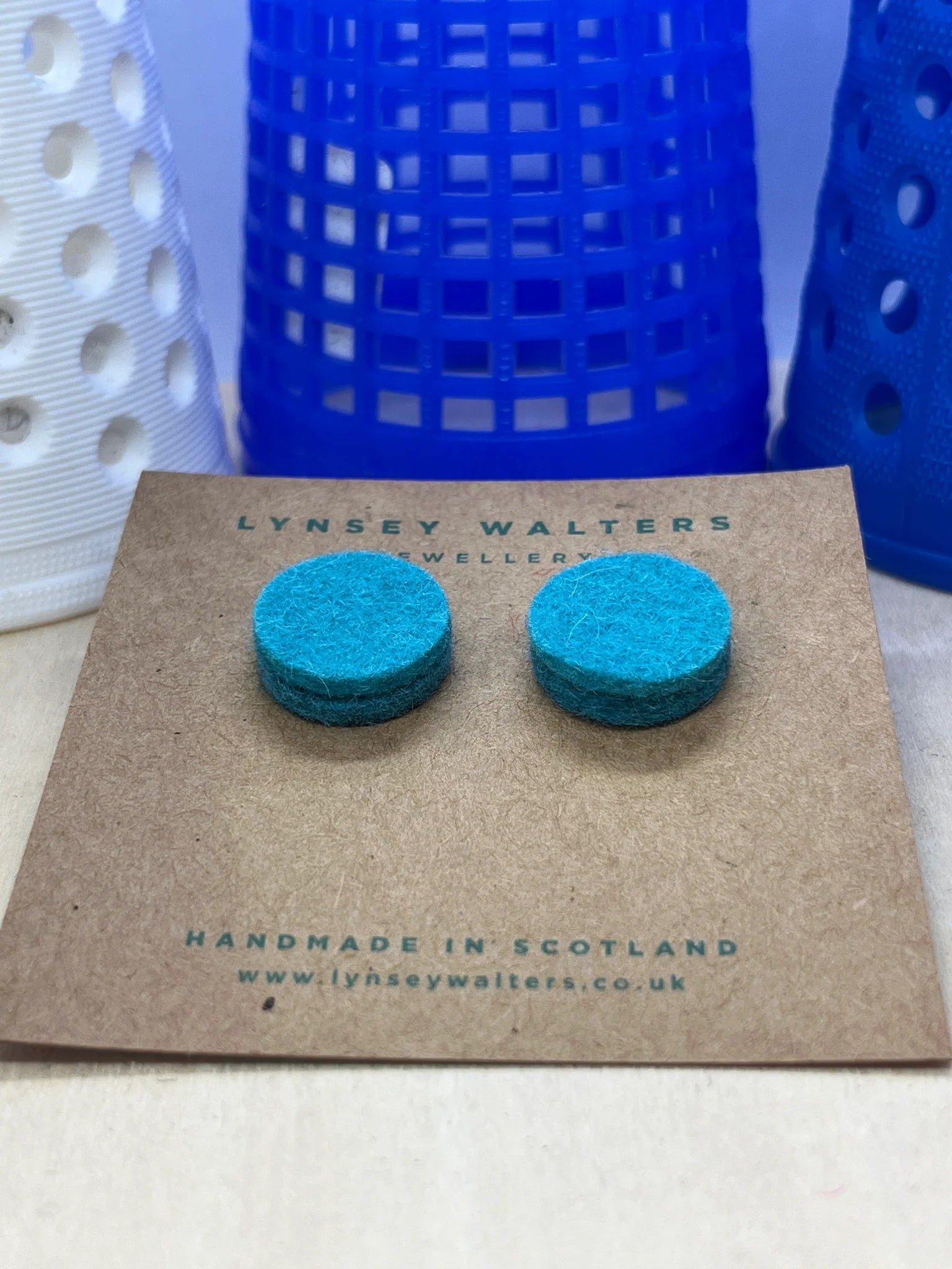 Pair of teal felt circle stud earrings displayed on a brown card.  Handmade in Scotland.