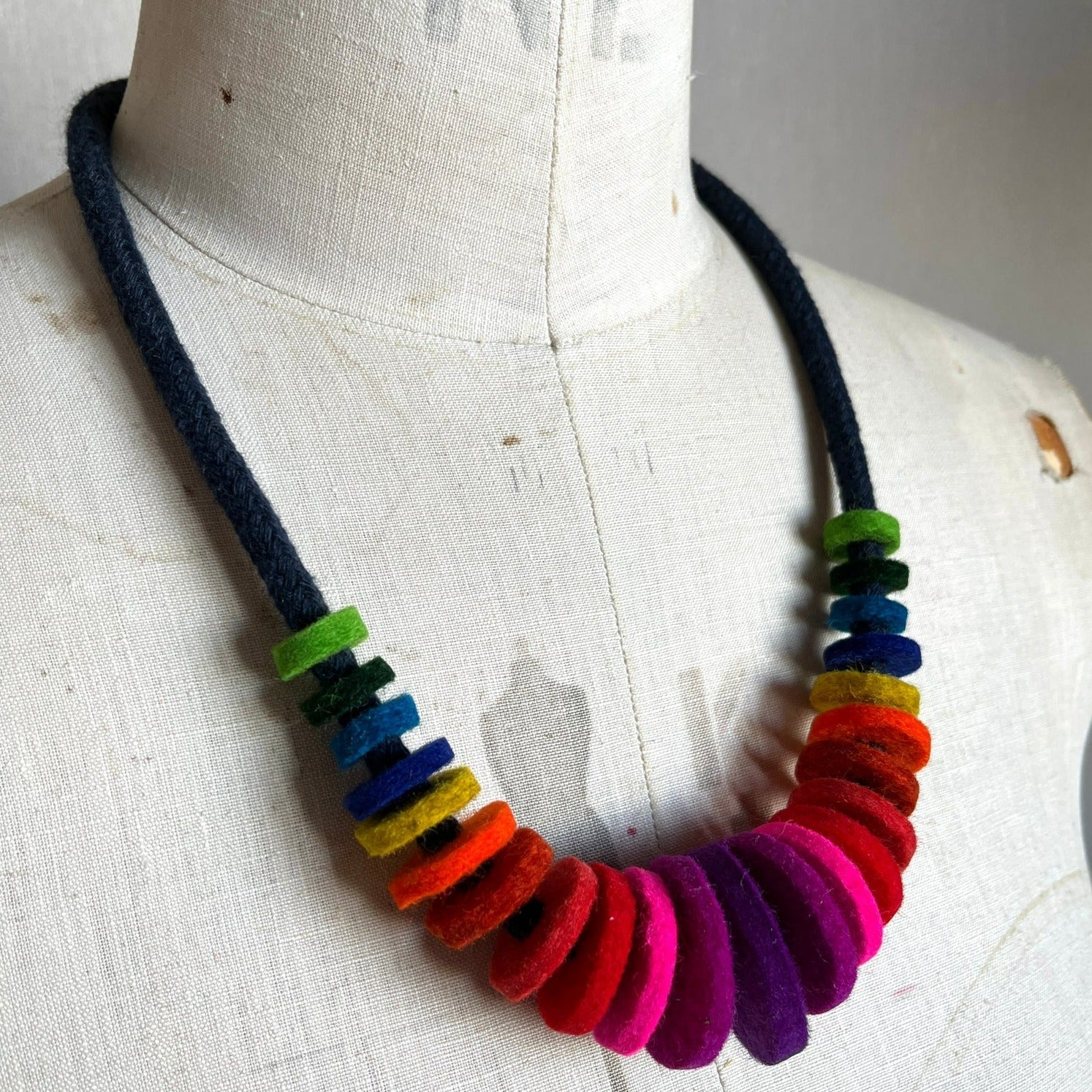 A colorful necklace made of merino wool industrial felt discs, displayed on a mannequin's neck.
