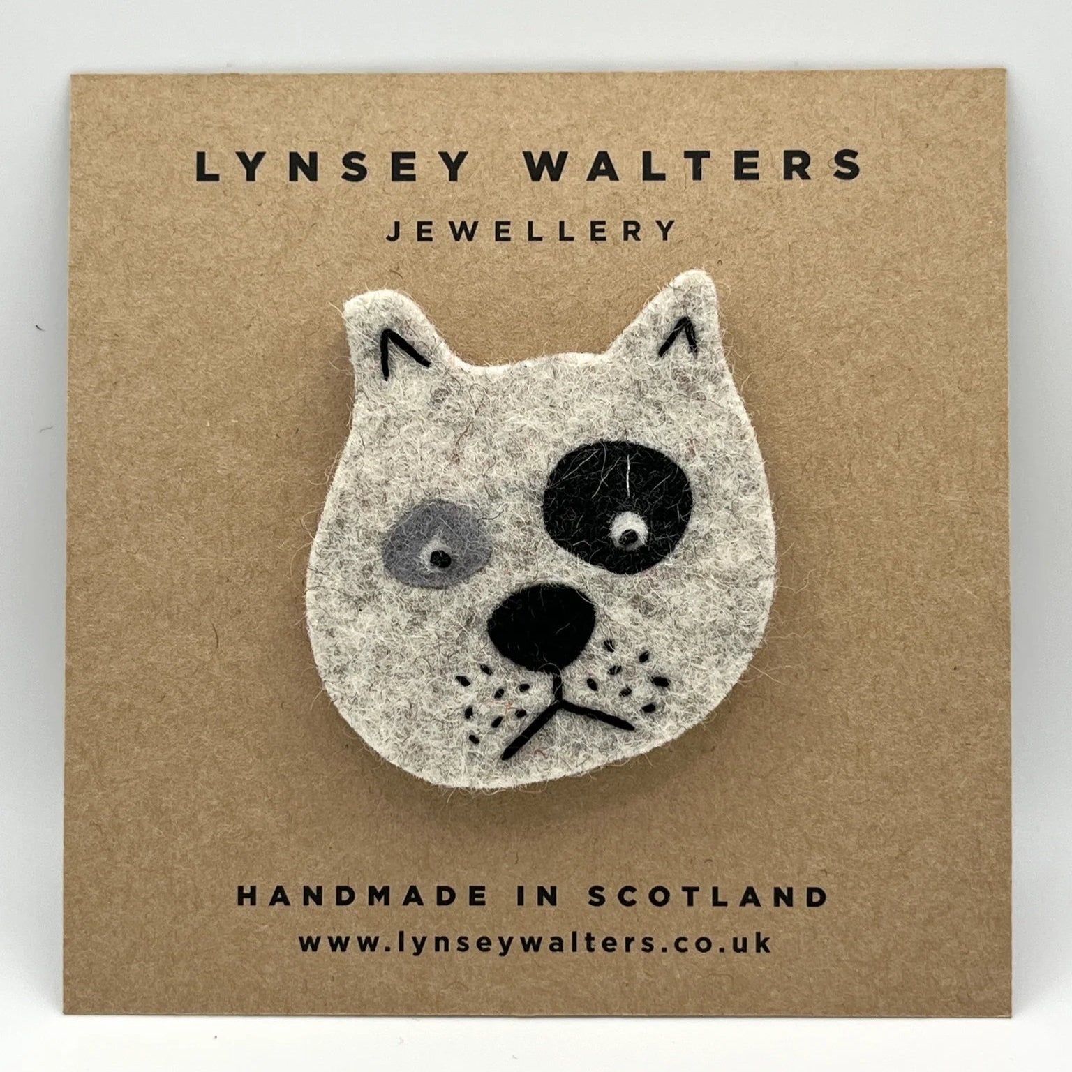 Handmade felt dog brooch, off-white with black markings.