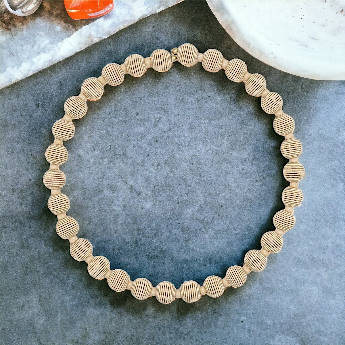Beige circular necklace with textured, ribbed beads.