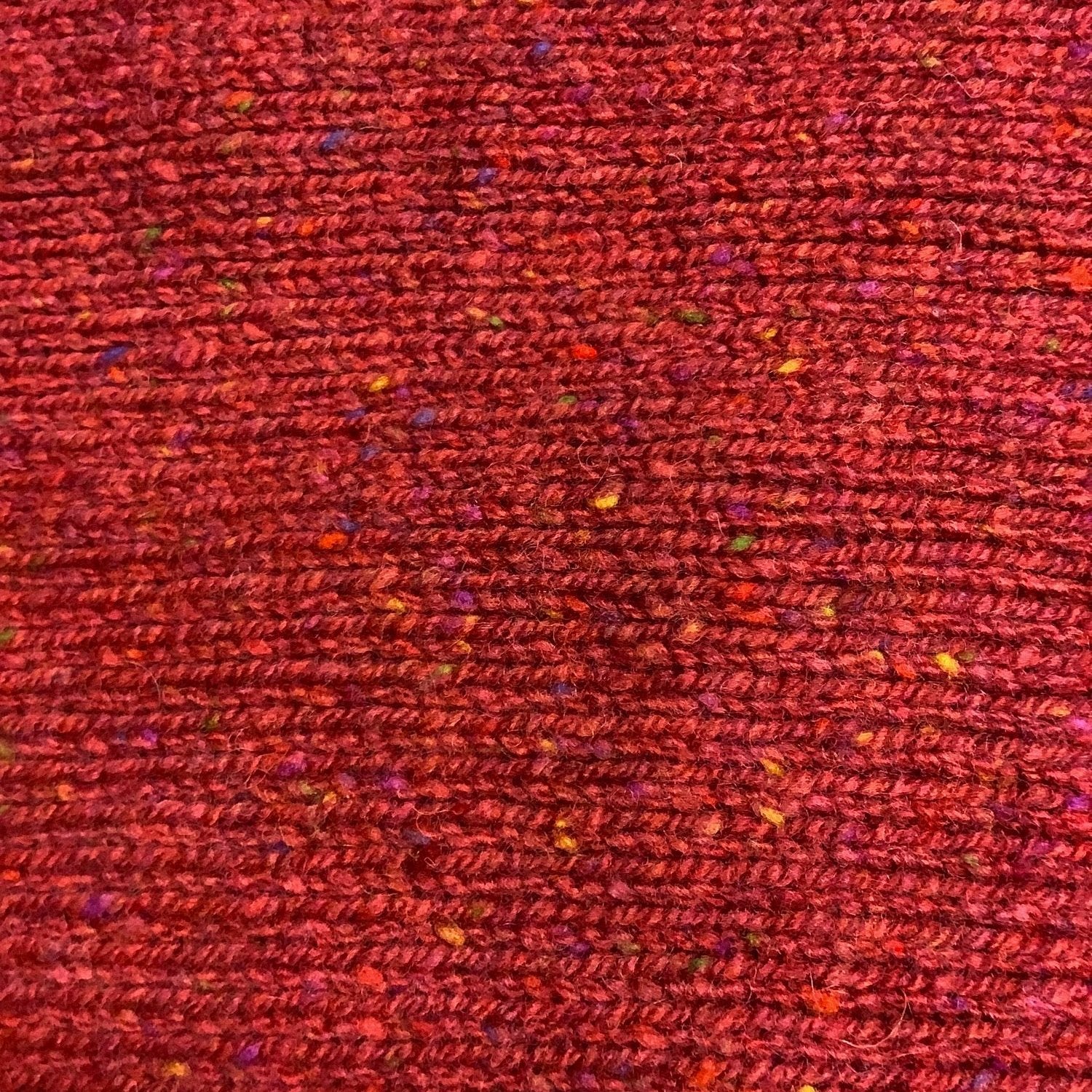 Close-up of a red speckled knit fabric with subtly variegated yarn.