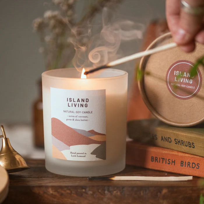 Frosted glass Island Living soy candle burning, with minimalist label featuring landscape design.