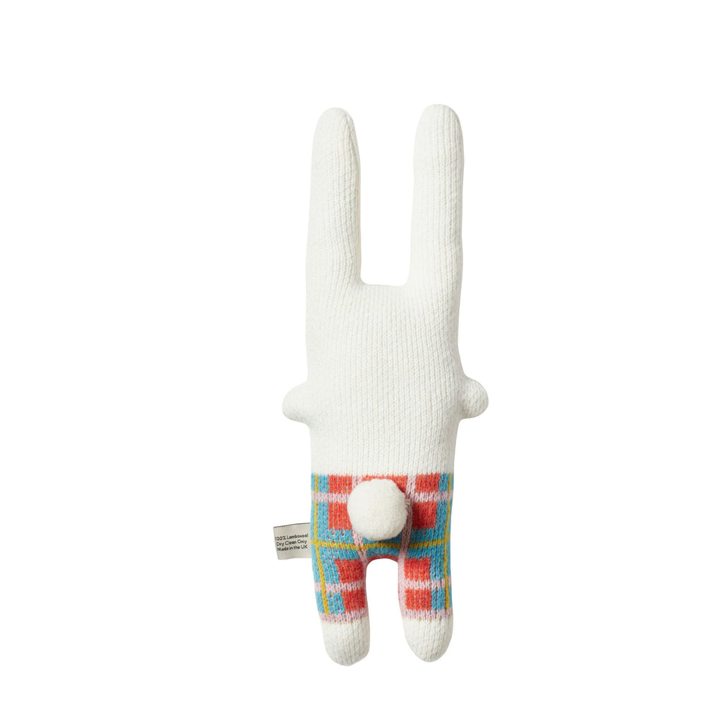 A white rabbit toy by Donna Wilson, with colorful checkered patterns in blue, orange, and pink on its legs.