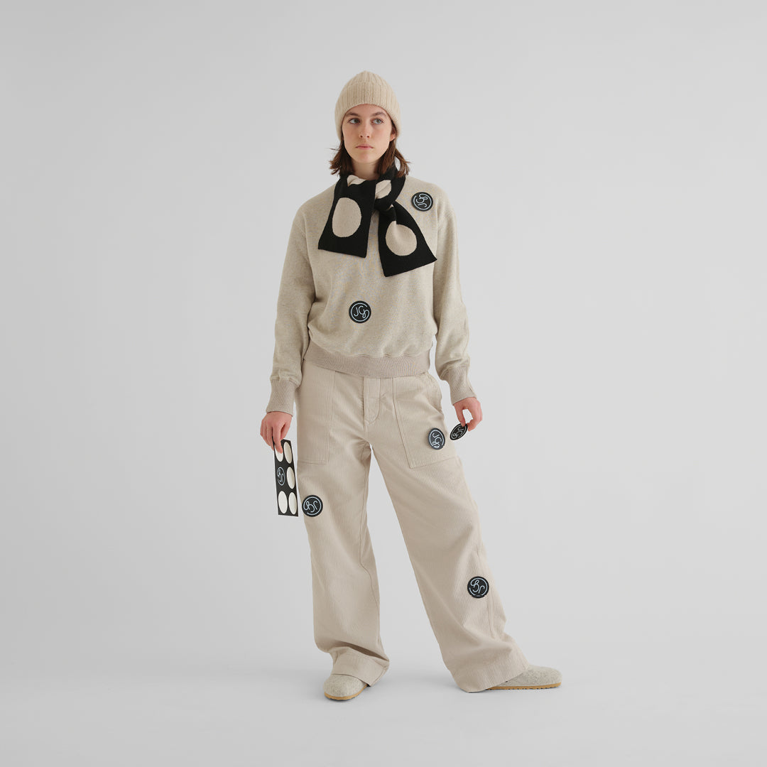 Beige corduroy pants and matching sweatshirt, adorned with black circular logo patches.