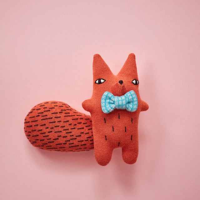 Stuffed fox toy with a blue bow tie on a pink background