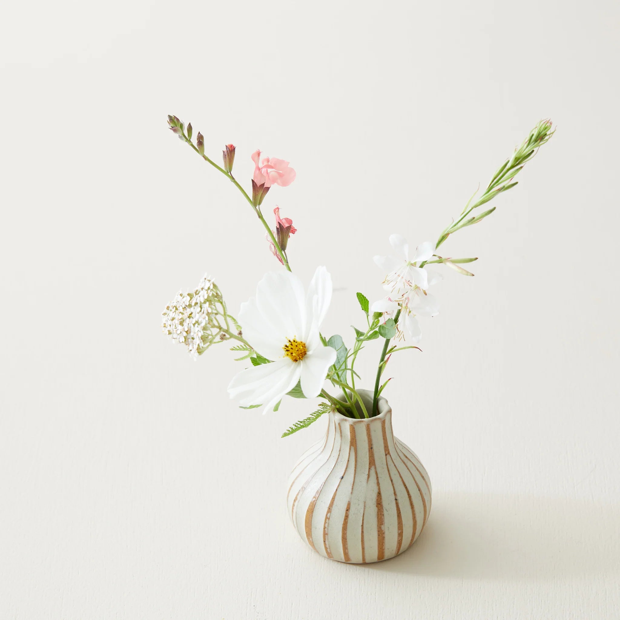 Small, bulbous vase with vertical gold stripes holds a bouquet of white and light pink flowers.