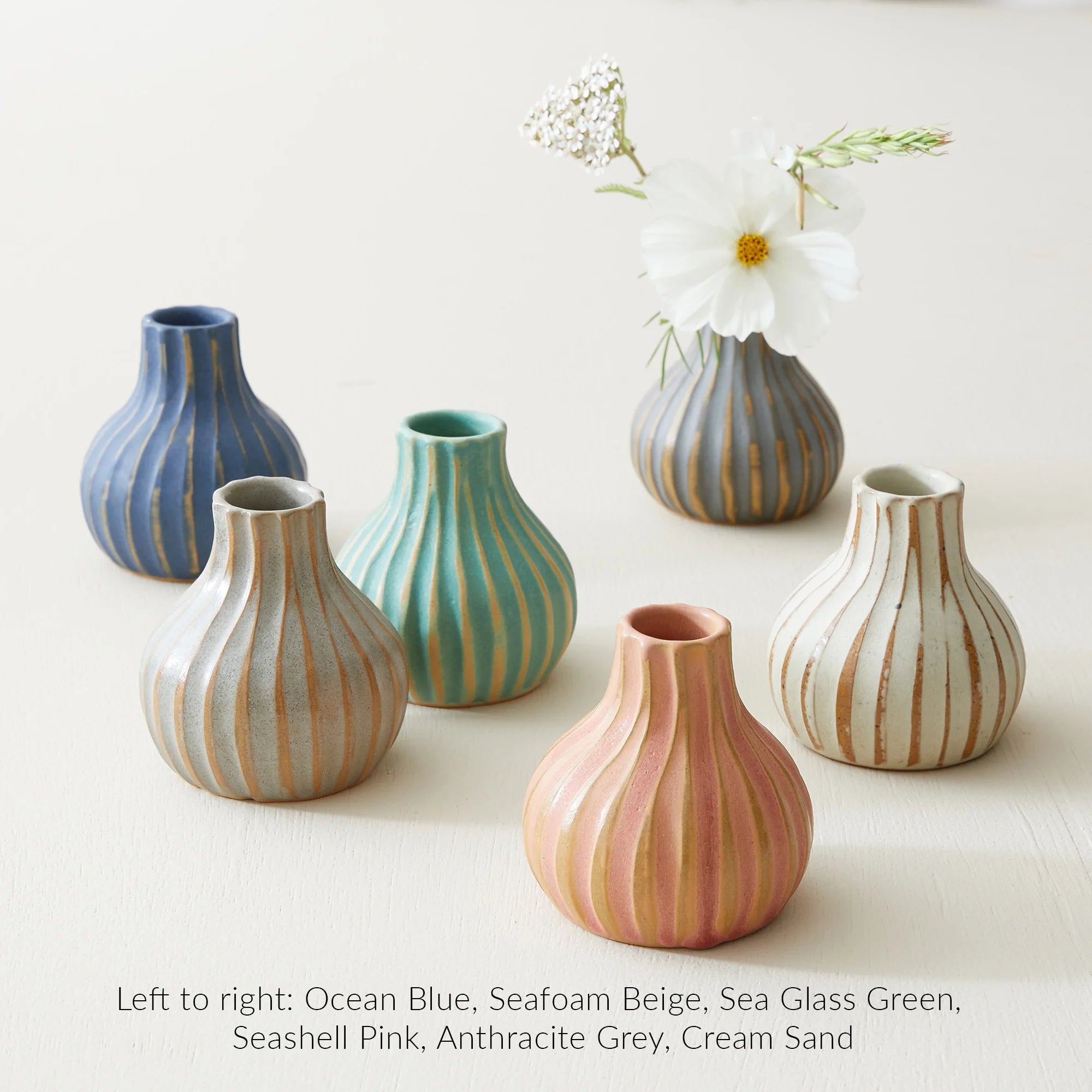 Five small, ribbed ceramic vases in various pastel colors with gold stripes.