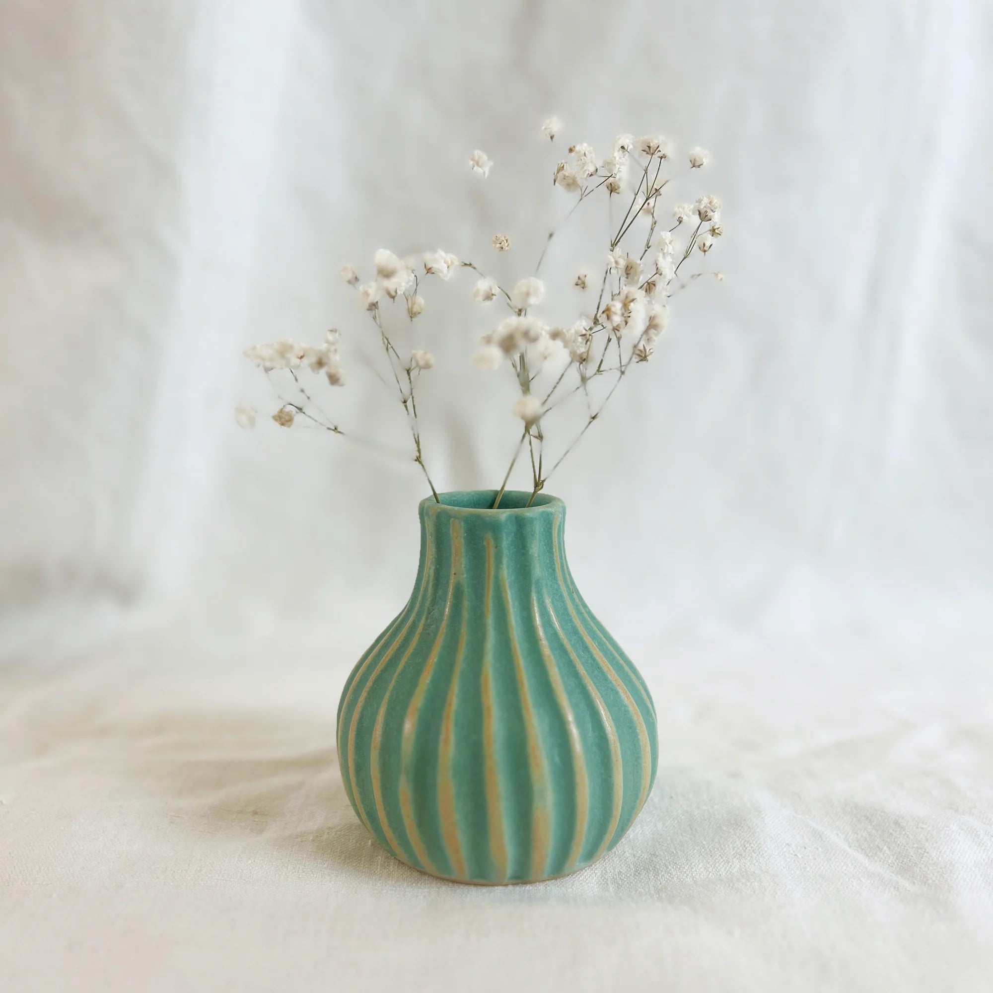 Small teal ceramic vase with vertical ribbed texture, holding a bunch of white baby's breath flowers.