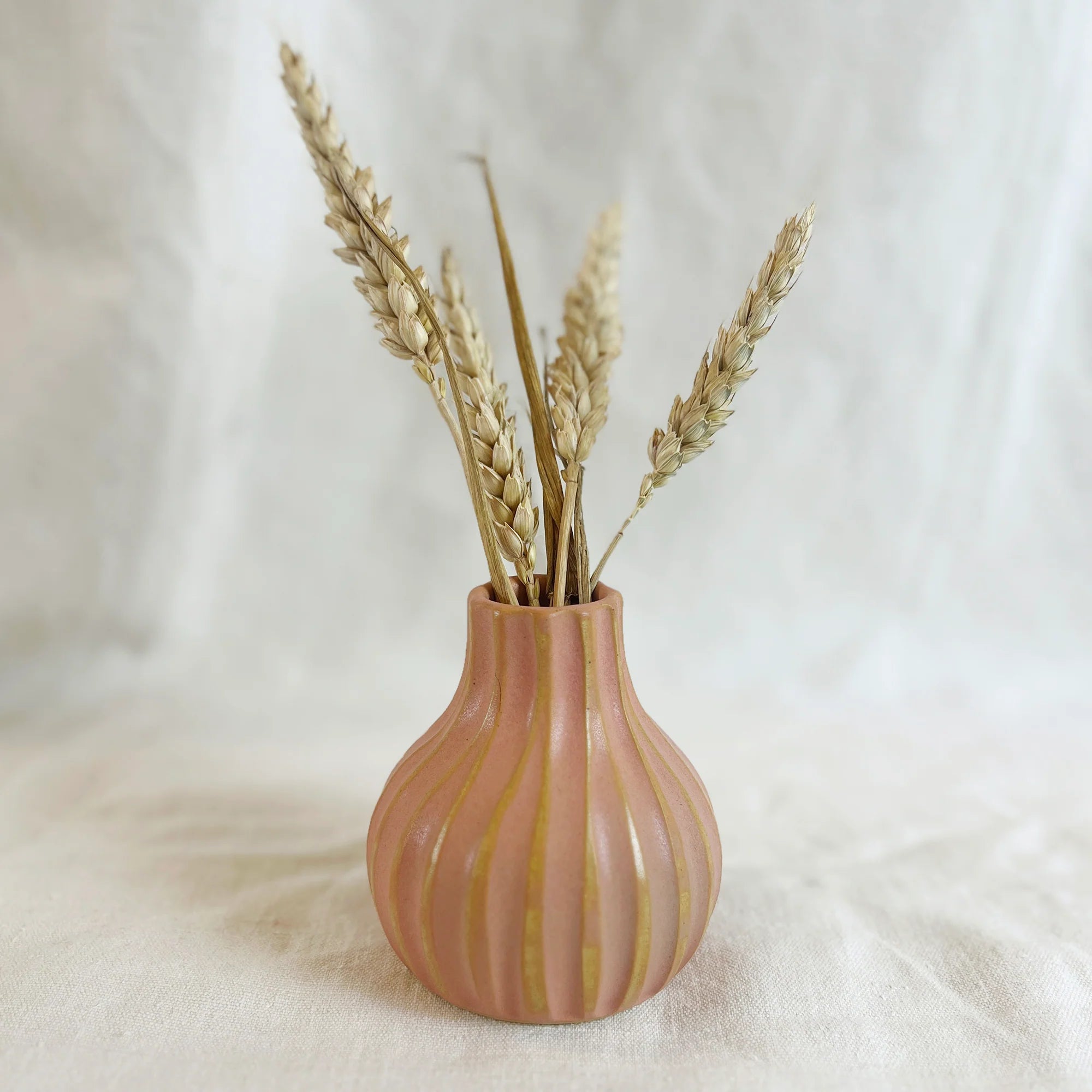Pink ceramic vase with vertical ribbed texture and gold accents, holding dried wheat stalks.