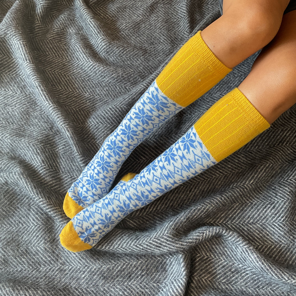 Pair of knee-high socks with a blue snowflake pattern and yellow cuffs.