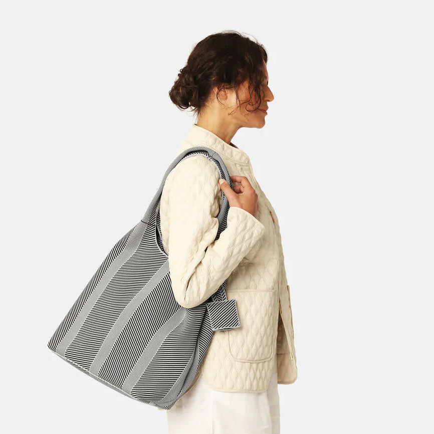 Woman carrying a gray striped tote bag on a white background