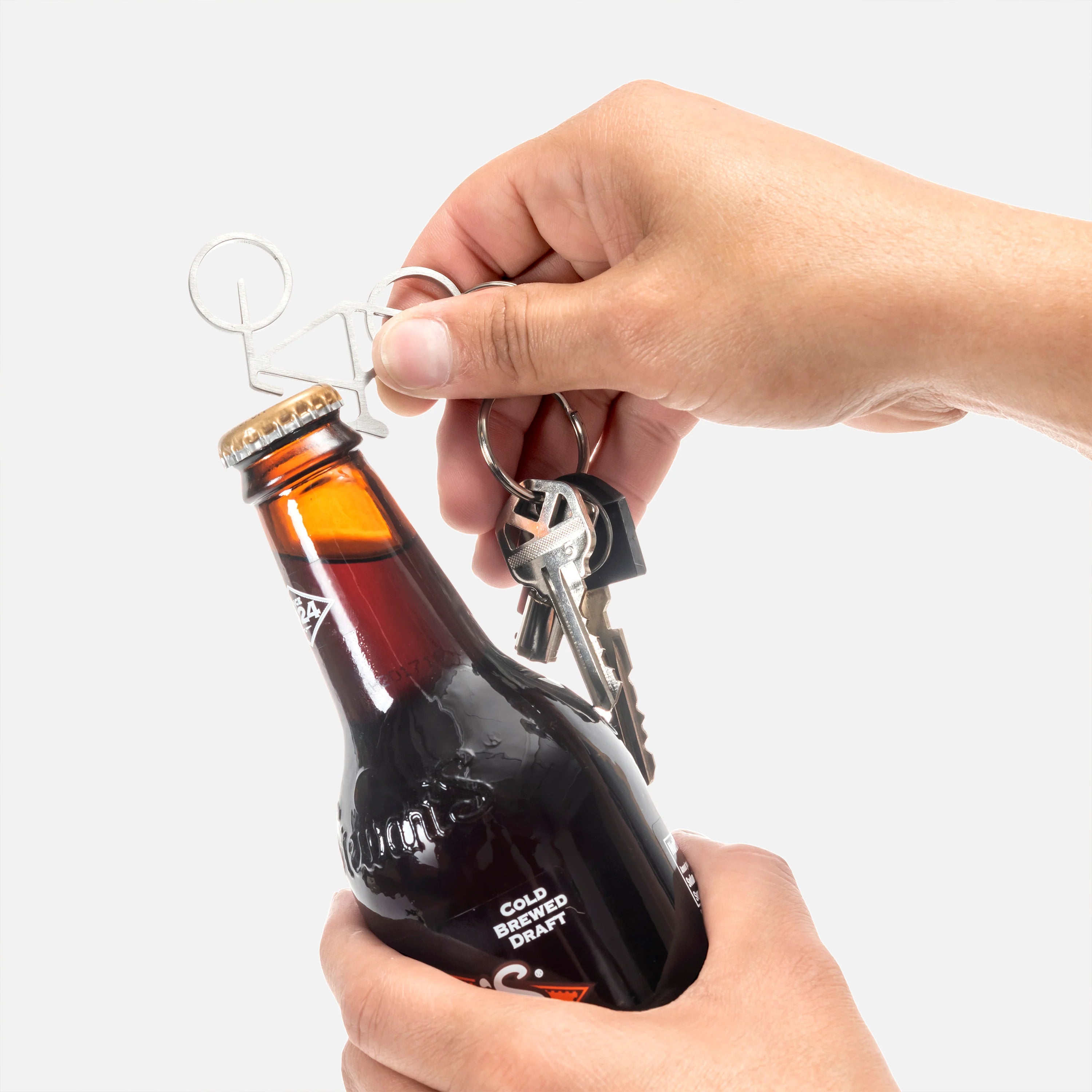 Bicycle-shaped bottle opener keychain opening a dark brown glass bottle.
