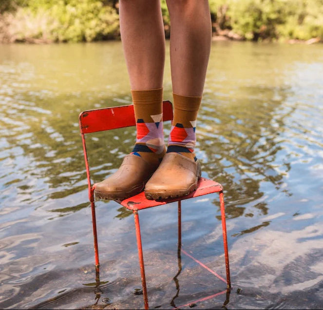 Person sitting on a red chair in water wearing colorful socks and brown shoes.