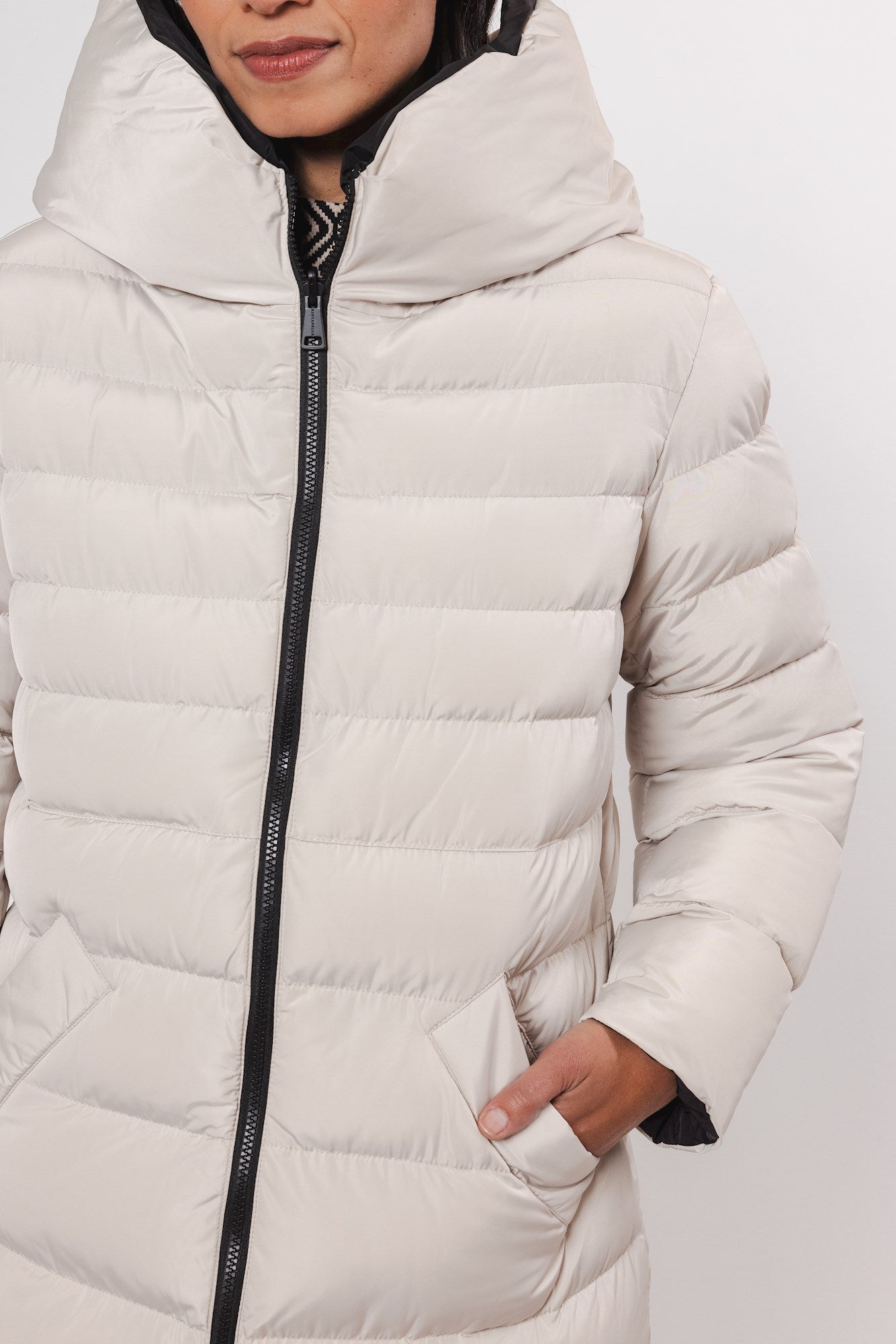 Beige quilted puffer coat with a large hood and black zipper.  Features a relaxed fit and front pockets.