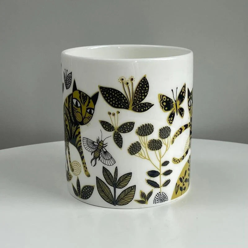 White mug with black and yellow floral and insect design on a gray background