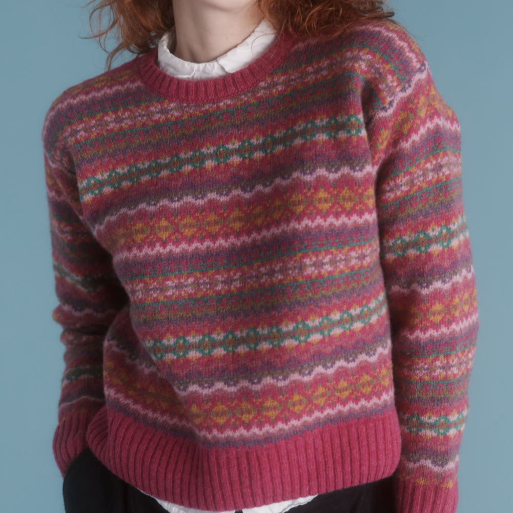 A woman wearing a multicolored fair isle jumper in shades of pink, red, green, and yellow.
