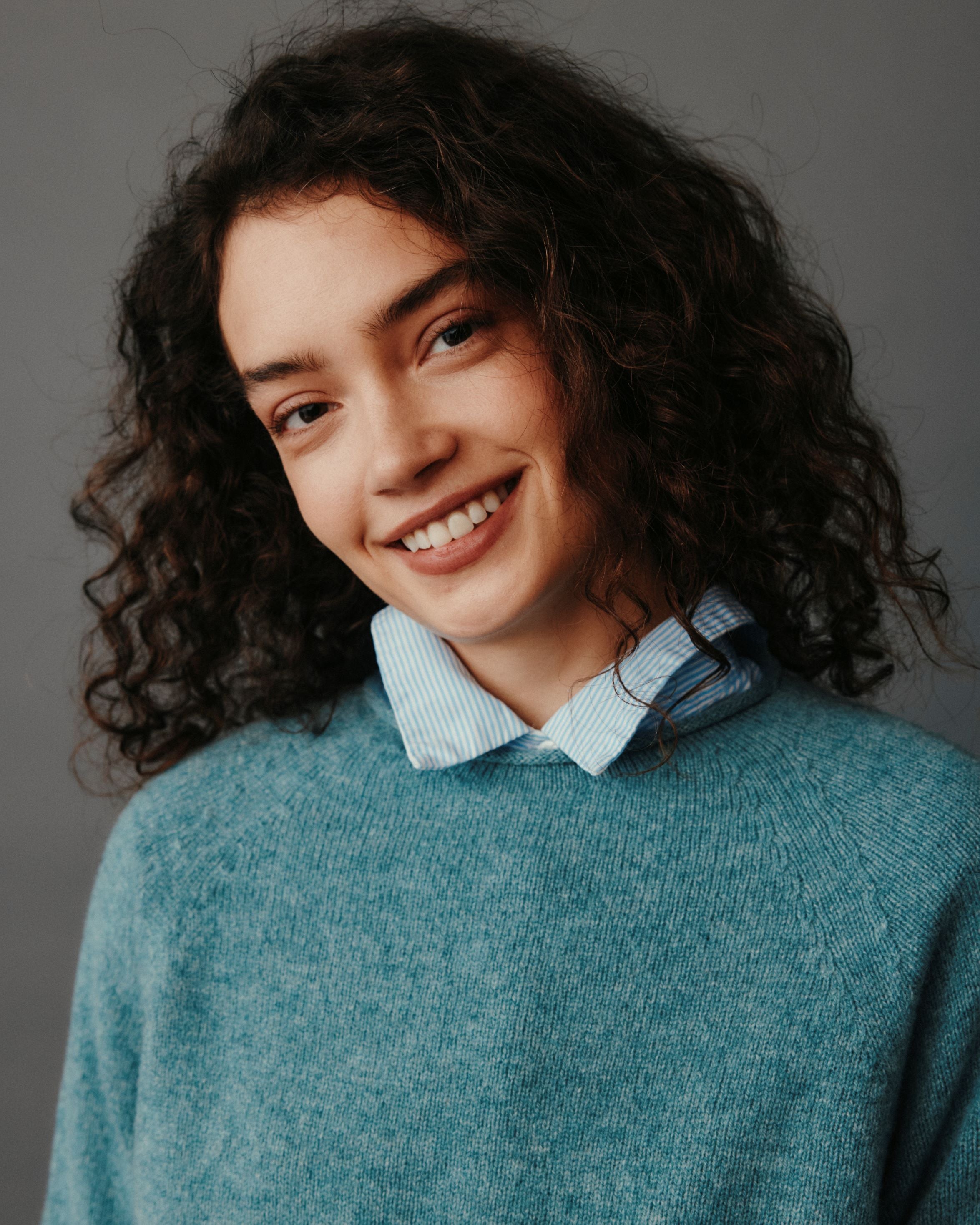 Person wearing a teal sweater over a light blue shirt against a gray background