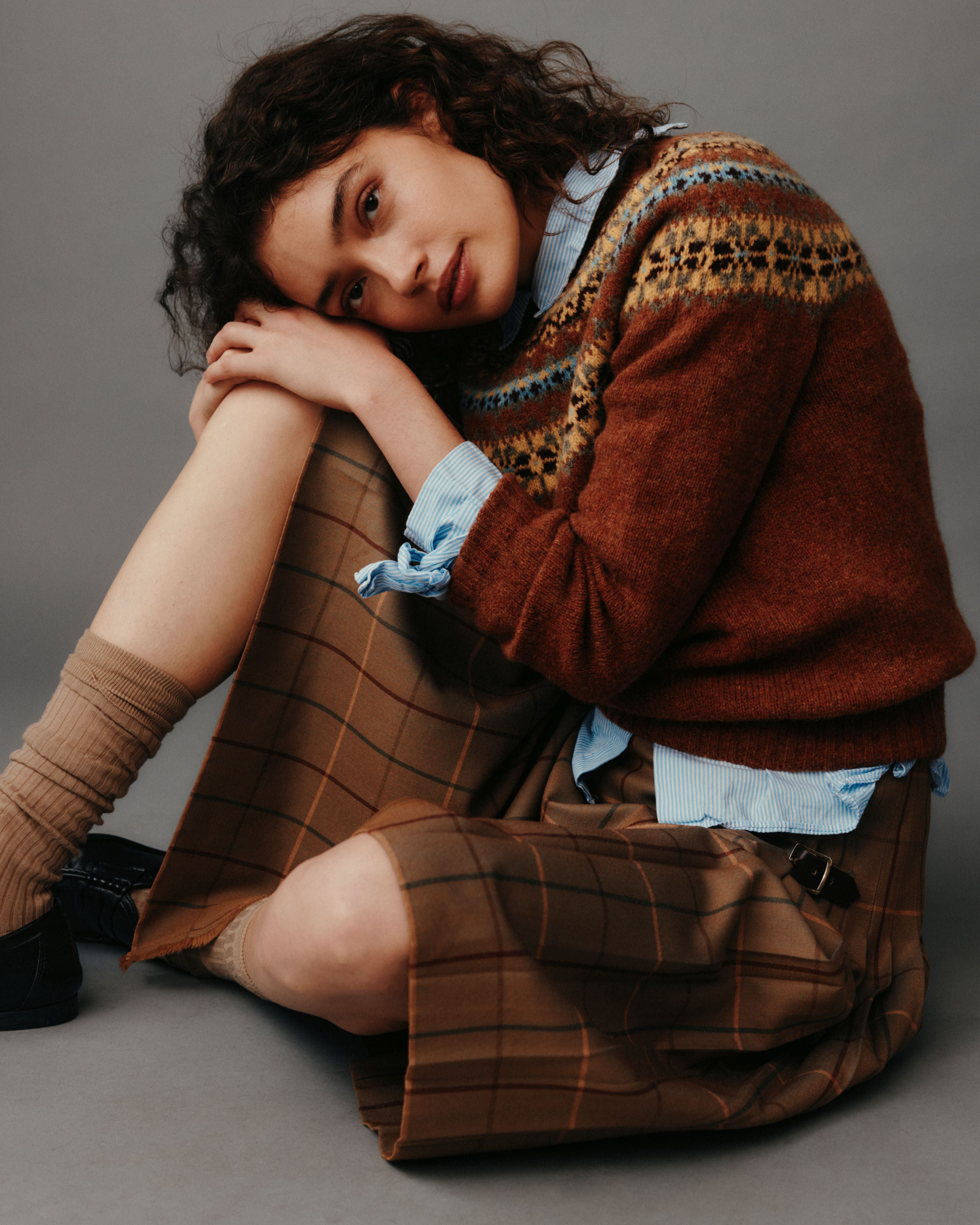 Woman wearing a brown plaid dress and sweater with a gray background