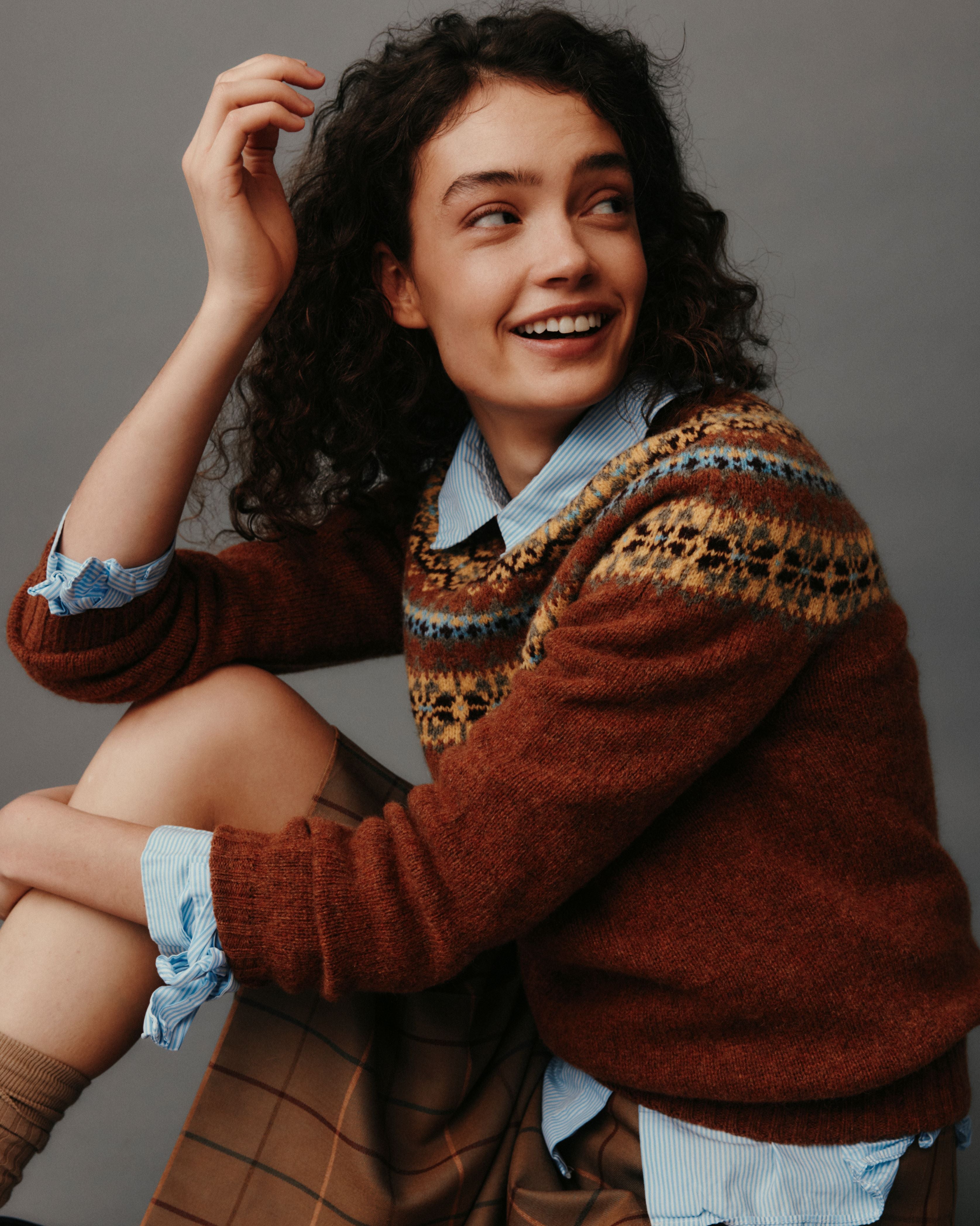 Woman wearing a patterned sweater sitting against a gray background