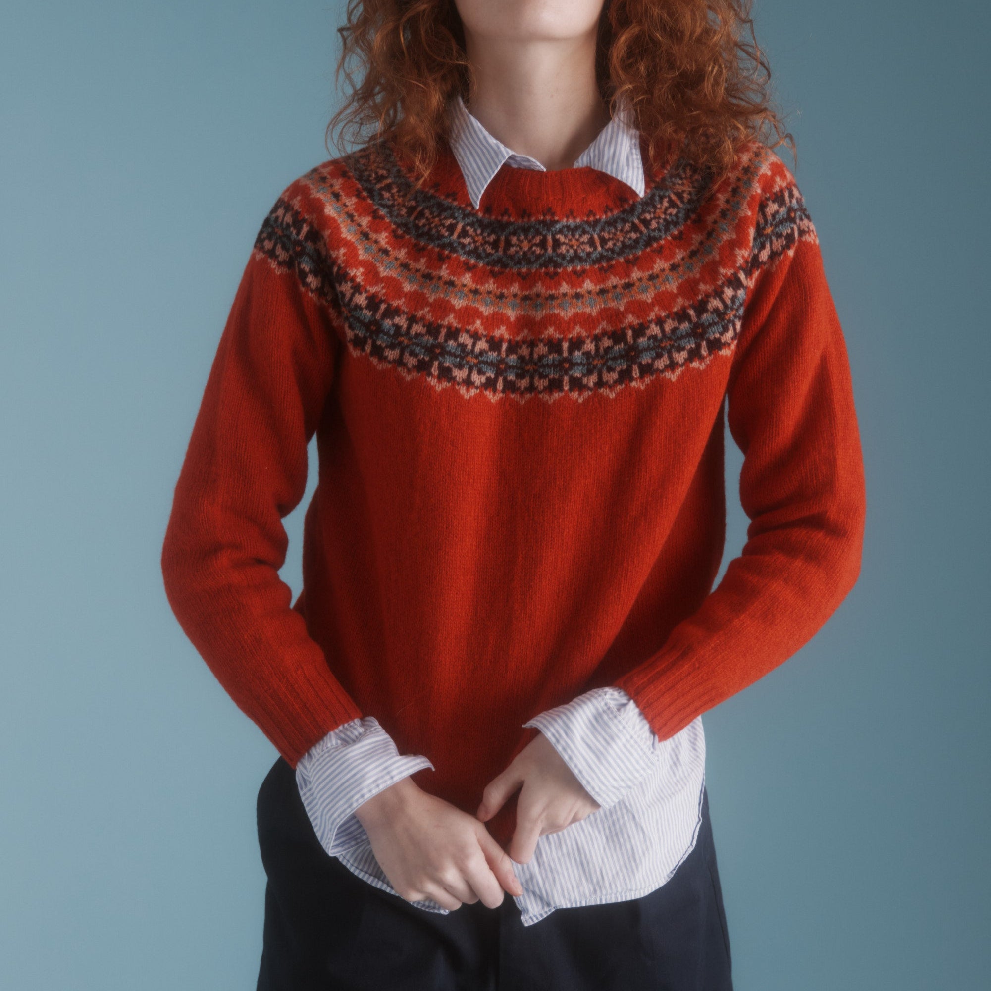 A woman wearing a red Fairisle jumper with a crew neckline, displayed against a neutral background.