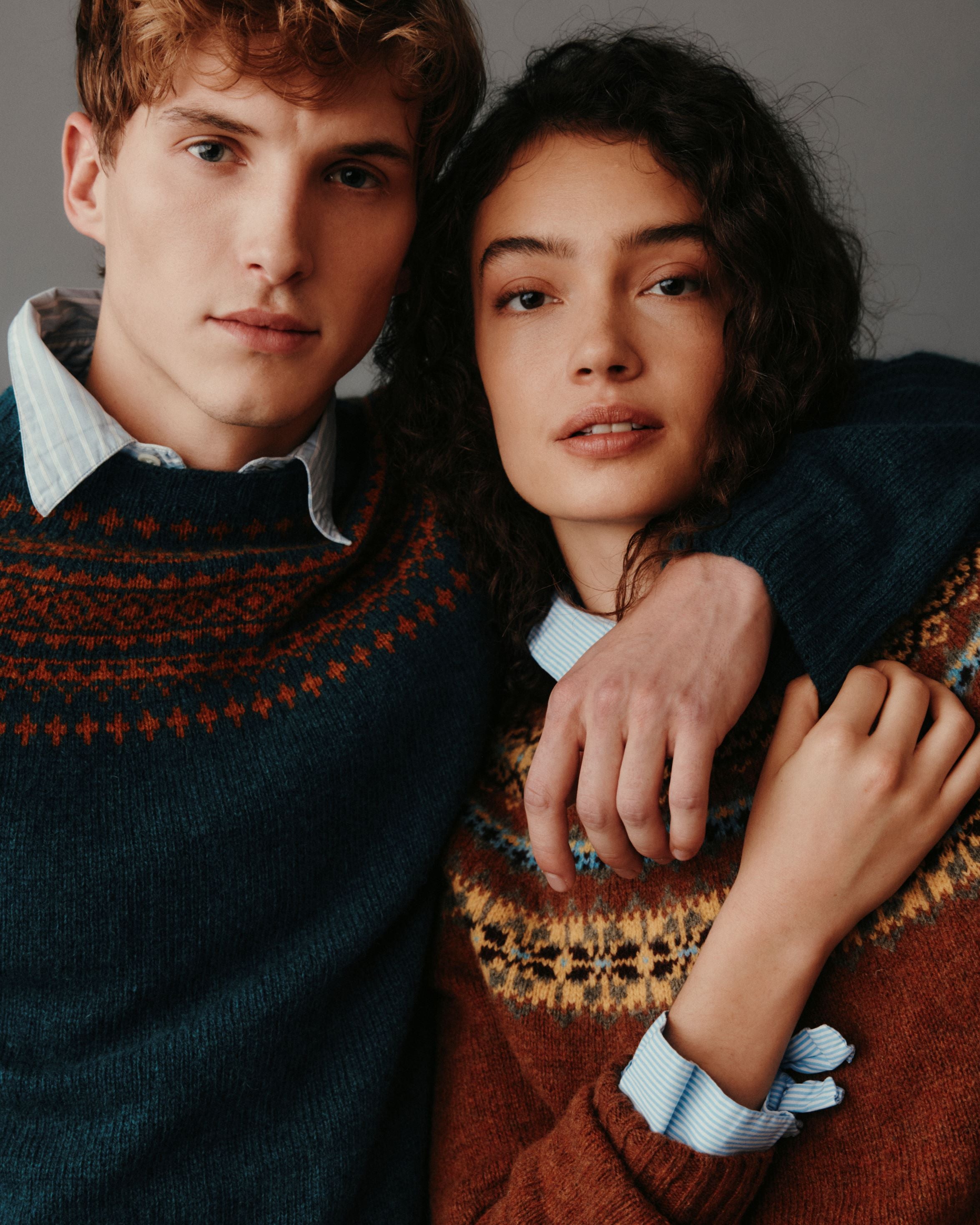 Two people wearing patterned sweaters posing closely together.