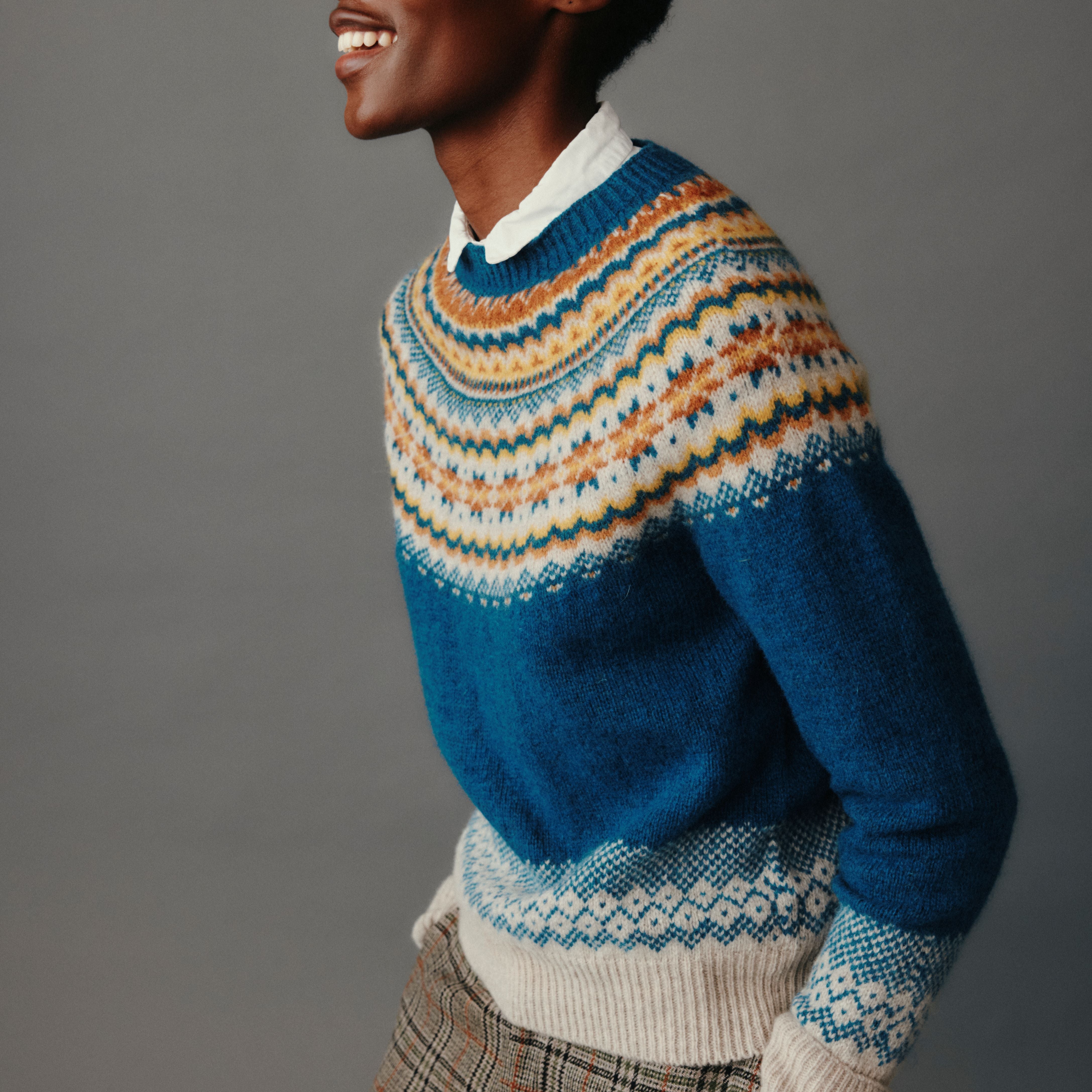 Person wearing a blue and multicolor patterned sweater against a gray background