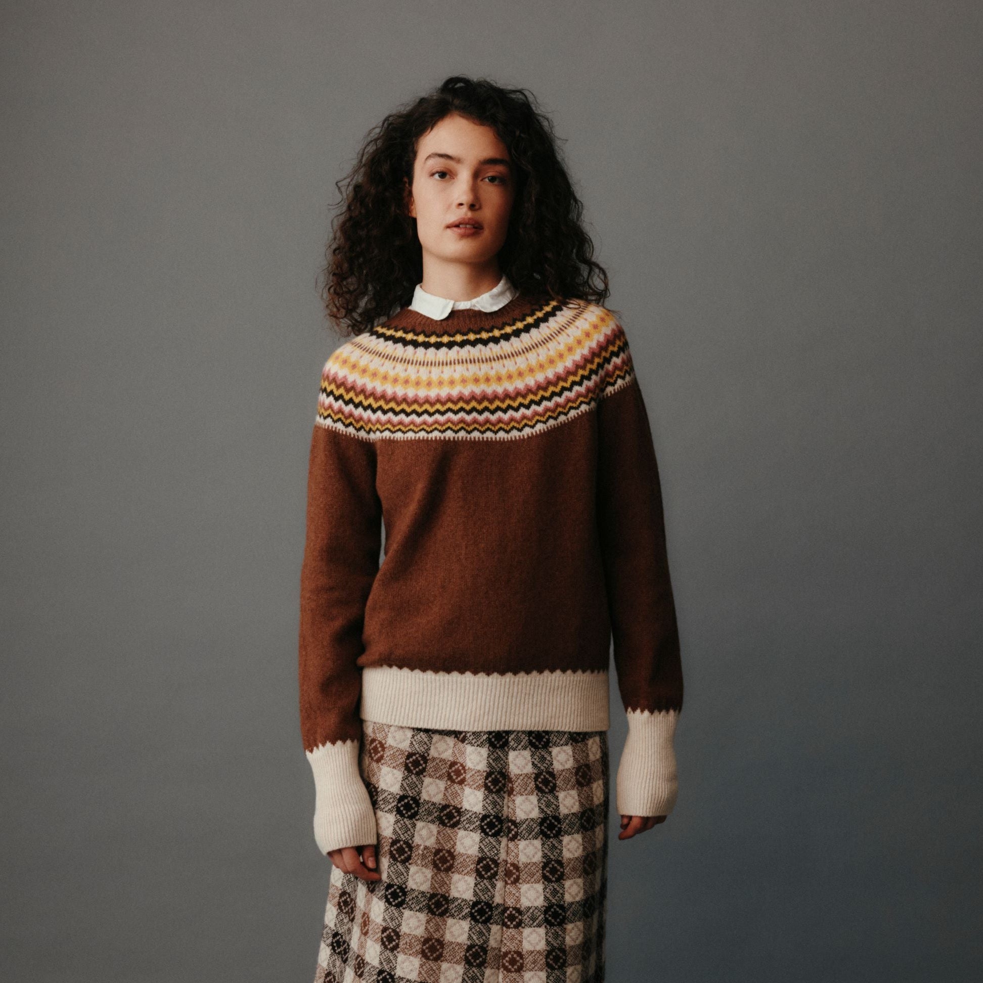Woman wearing a patterned sweater and plaid skirt against a gray background
