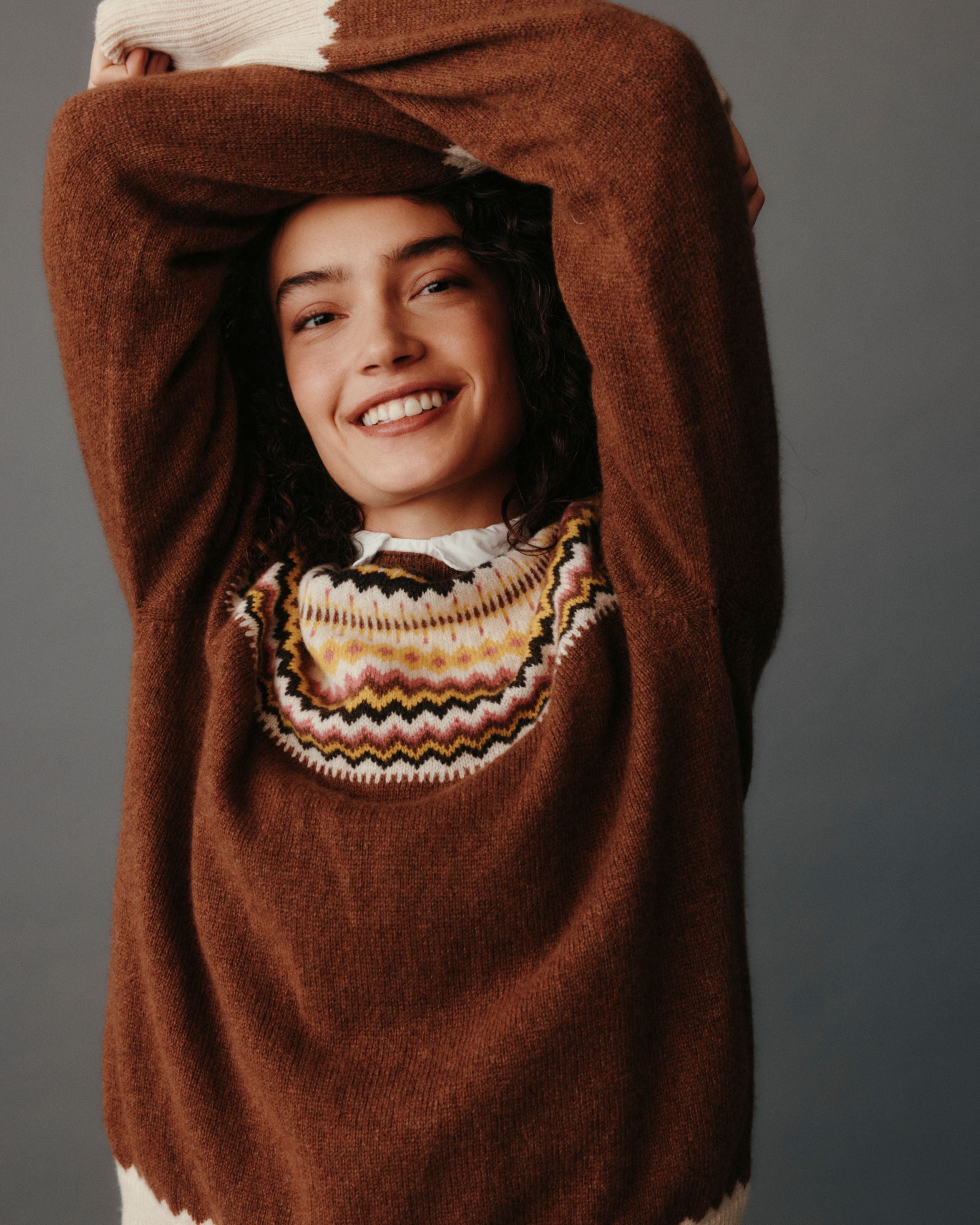 Person wearing a brown sweater with a patterned collar against a gray background