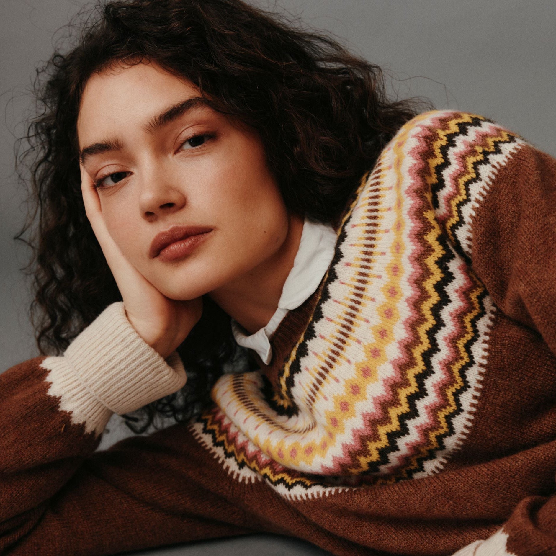 Woman wearing a brown sweater with a patterned collar against a gray background