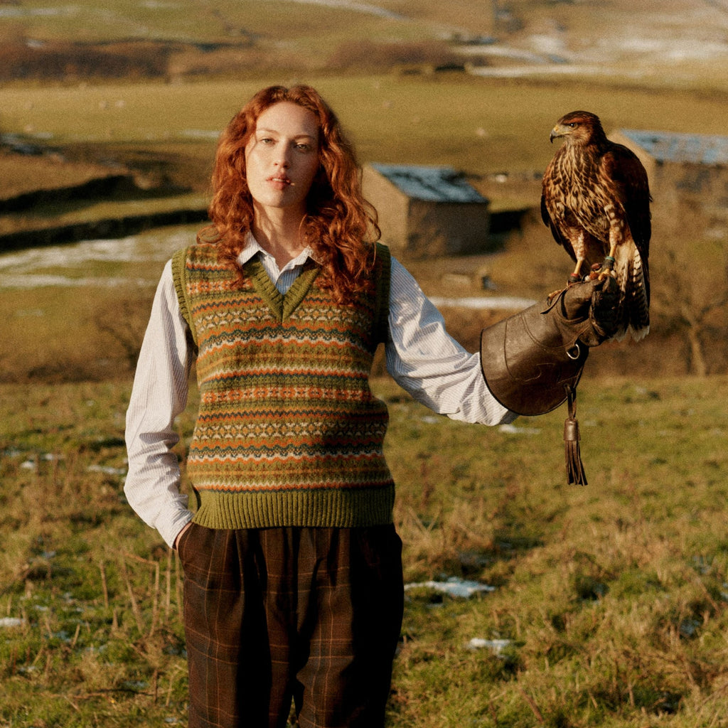 a red haired female model holding a bird of prey on an outstretched arm, wearing a Harley of Scotland Fairisle Slipover - Olive Grove