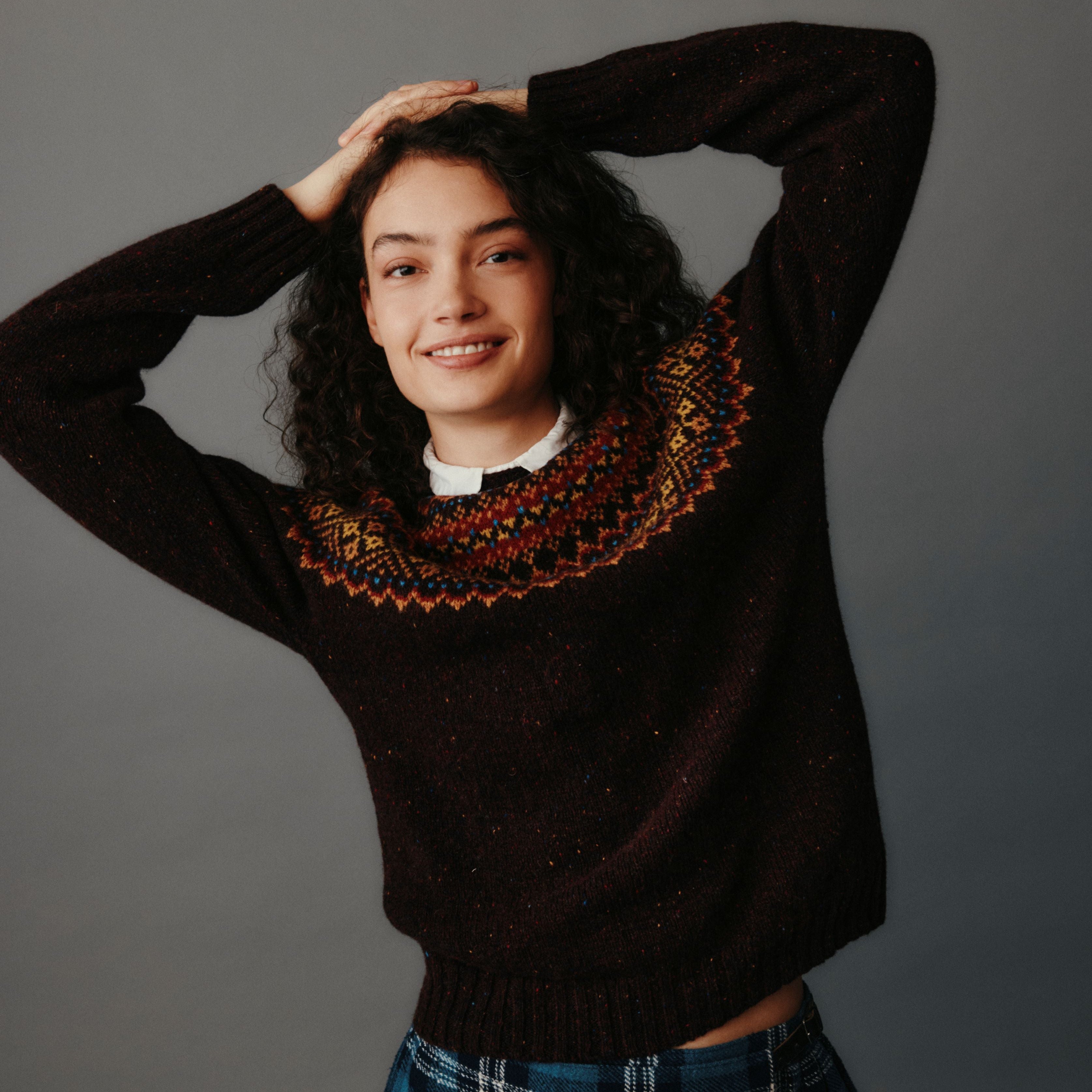 Woman wearing a dark sweater with a patterned neckline against a gray background