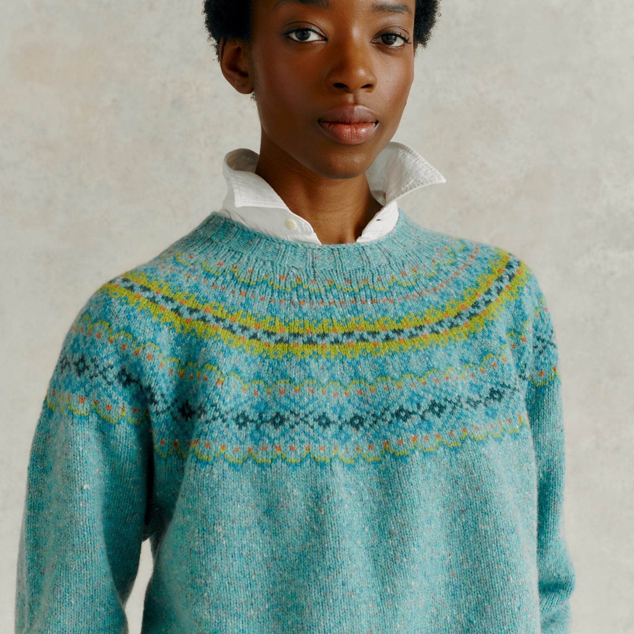 Teal crewneck sweater with a colorful Fair Isle yoke pattern. The sweater is knit and appears to be made of a soft yarn.