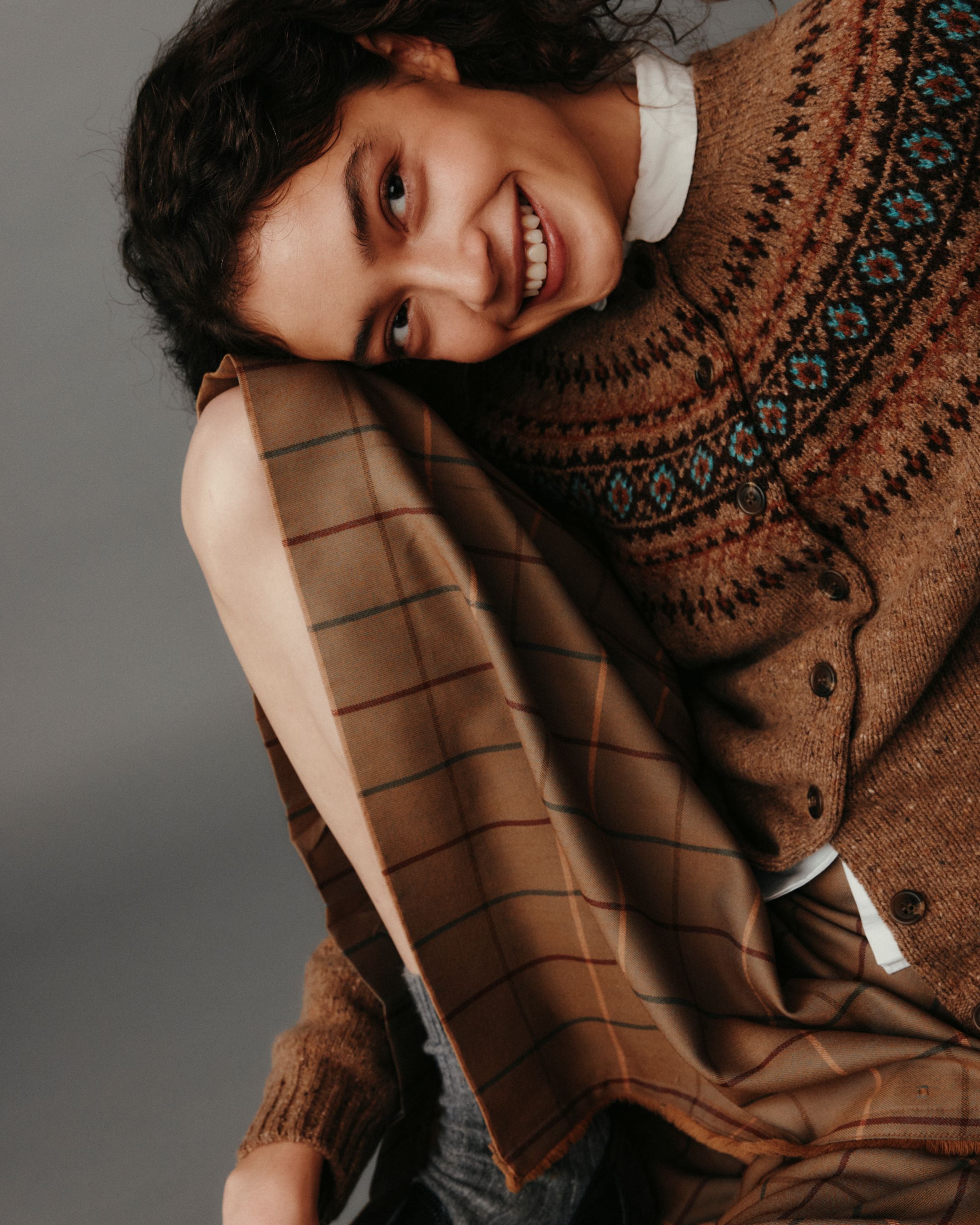 Person wearing a brown patterned sweater and plaid scarf against a gray background
