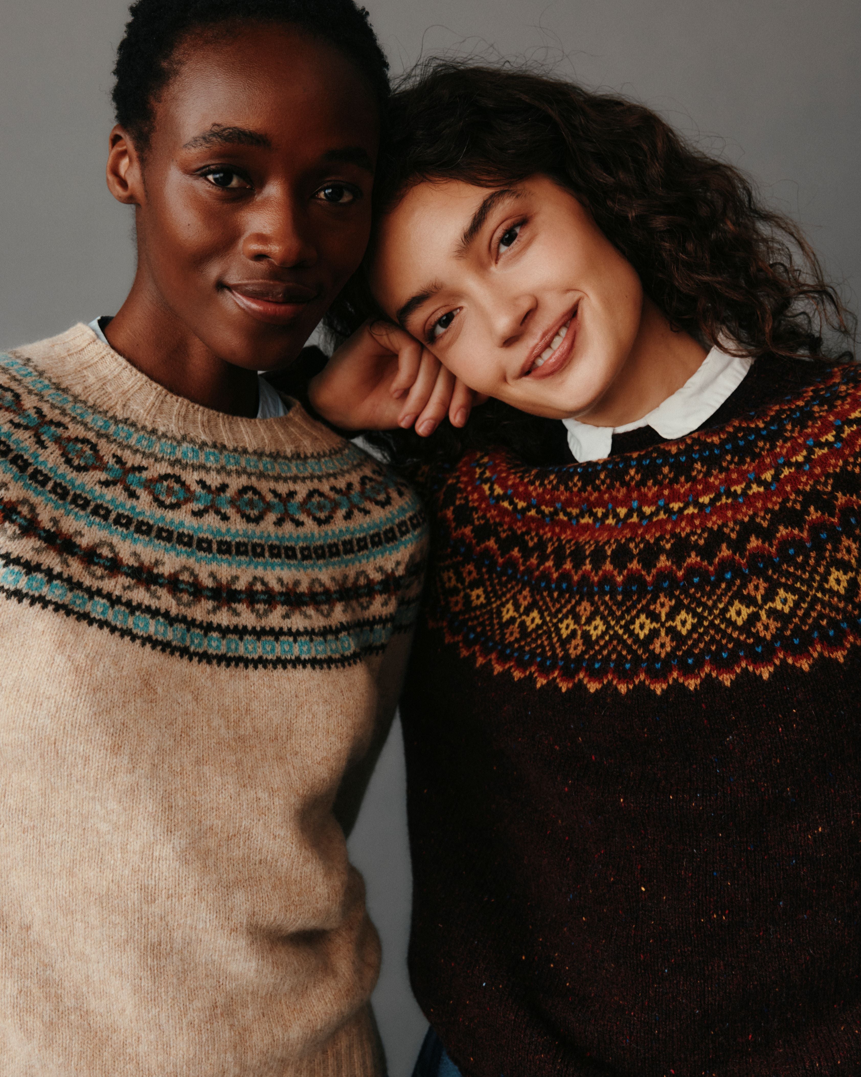 Two people wearing patterned sweaters against a neutral background