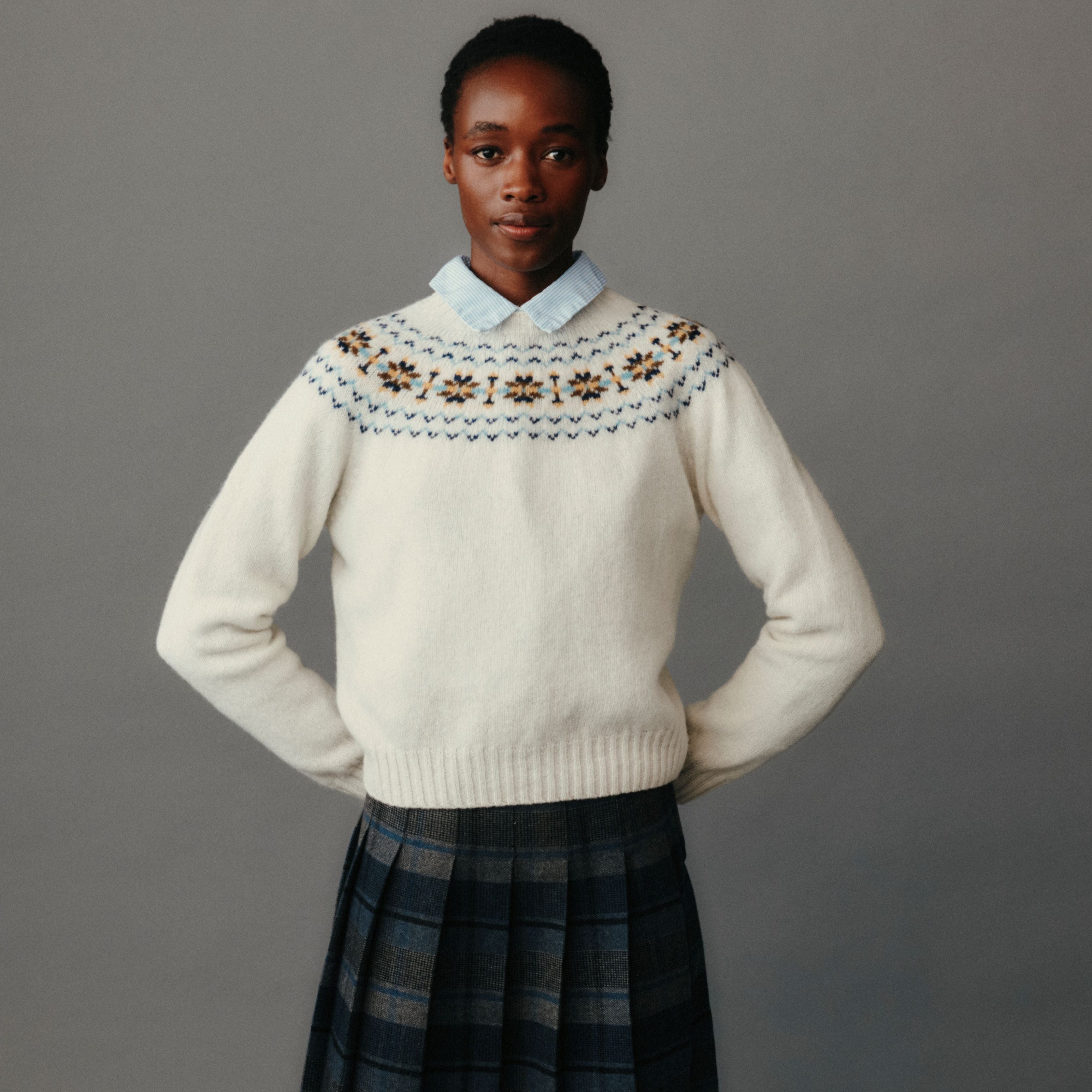 Person wearing a cream-colored sweater with a patterned collar against a gray background