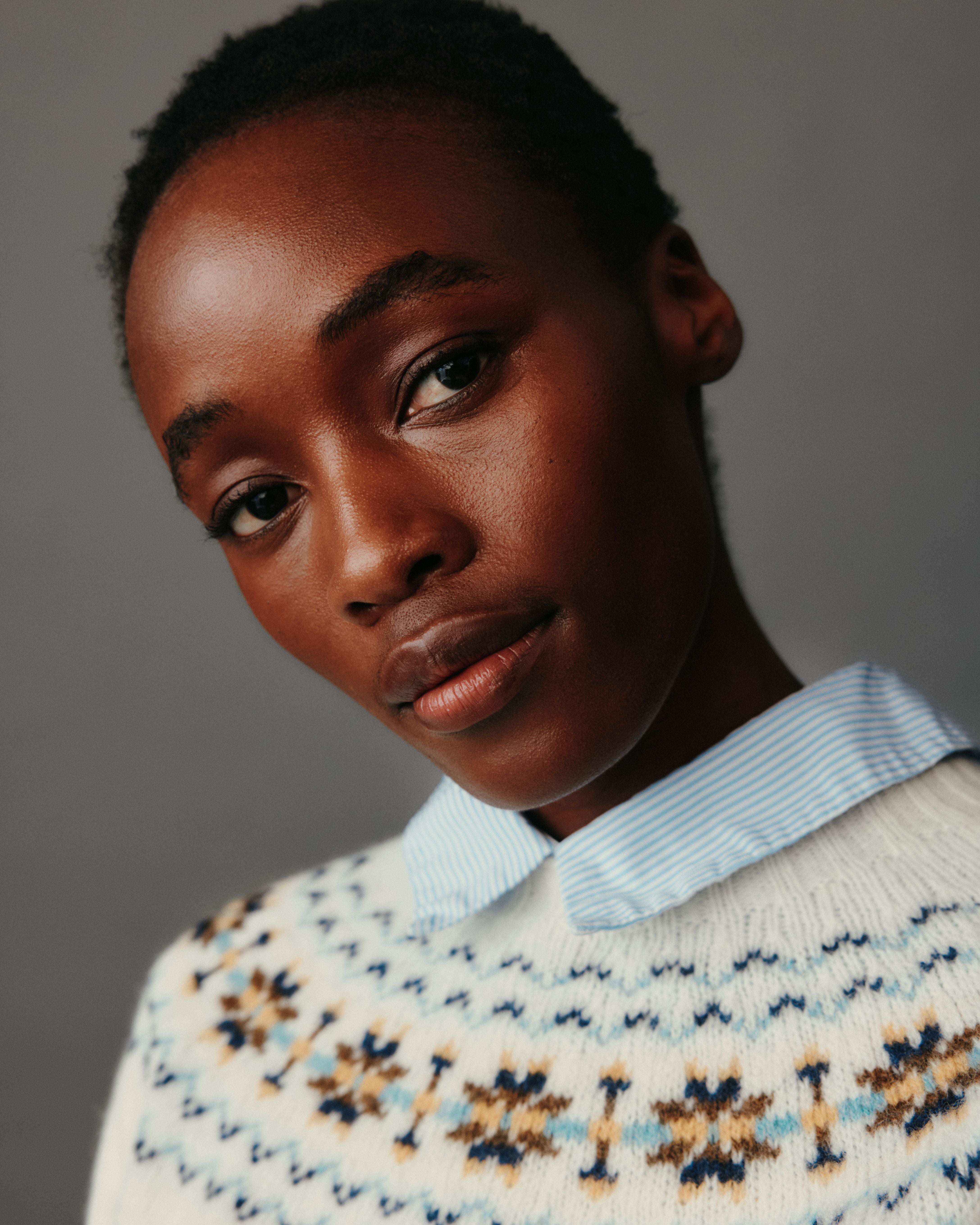Person wearing a patterned sweater with a light blue collar against a gray background
