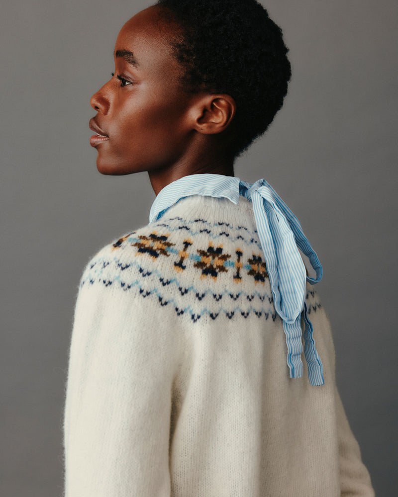 Person wearing a cream-colored sweater with a patterned yoke against a gray background