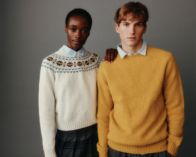 Two people wearing patterned sweaters against a gray background