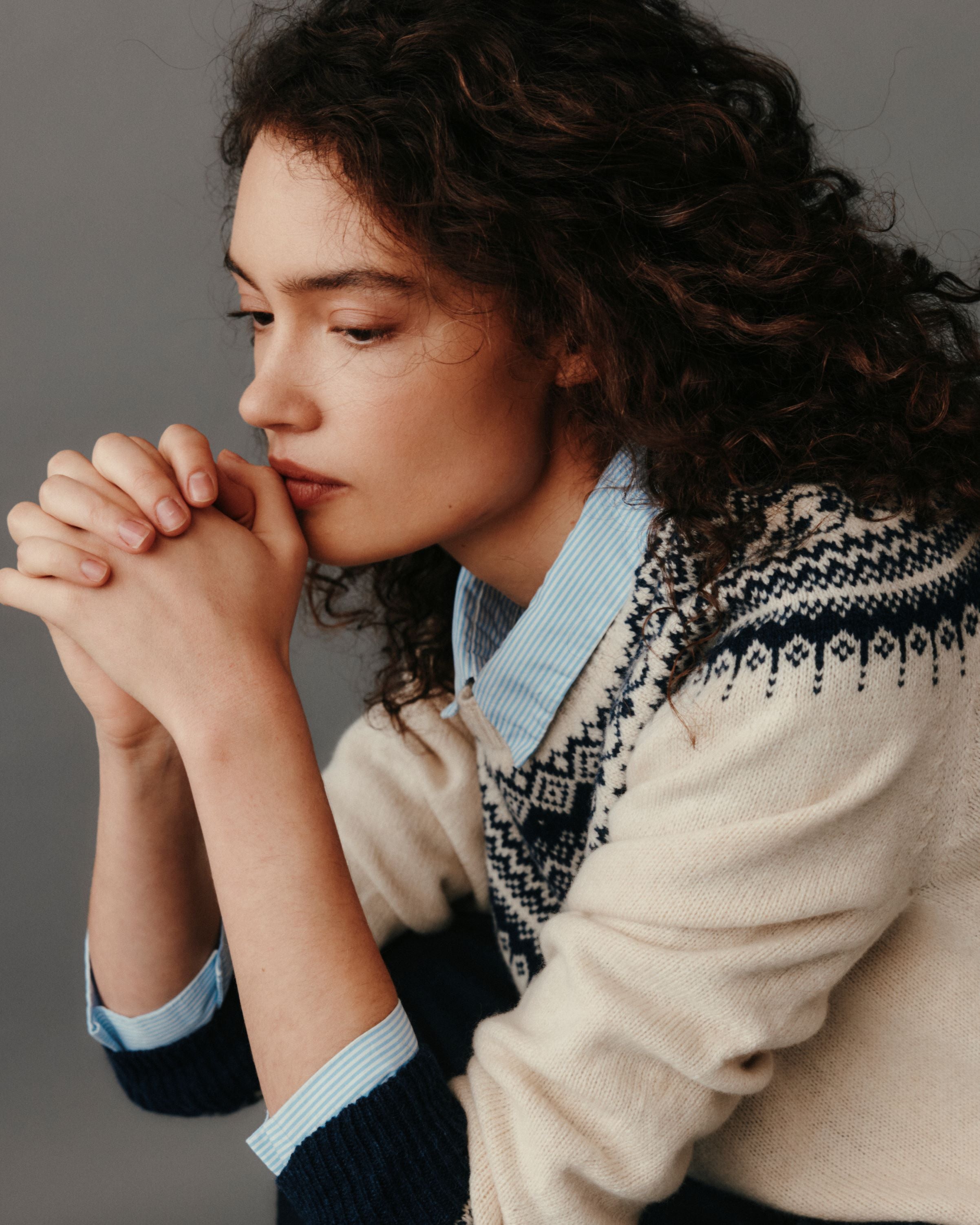 Woman wearing a patterned sweater with her hands clasped together against a neutral background