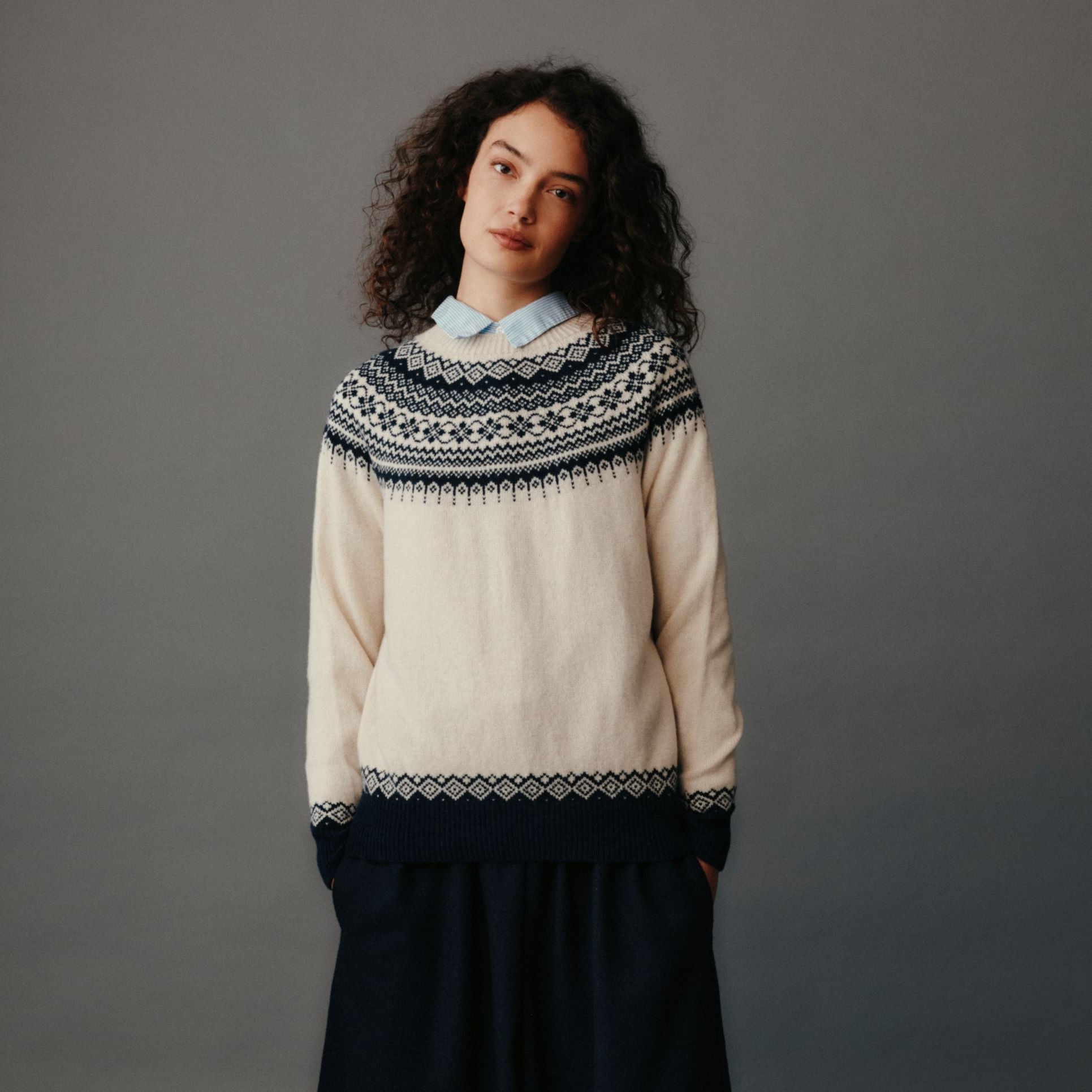 Person wearing a cream sweater with a patterned collar and black wide-leg pants on a gray background