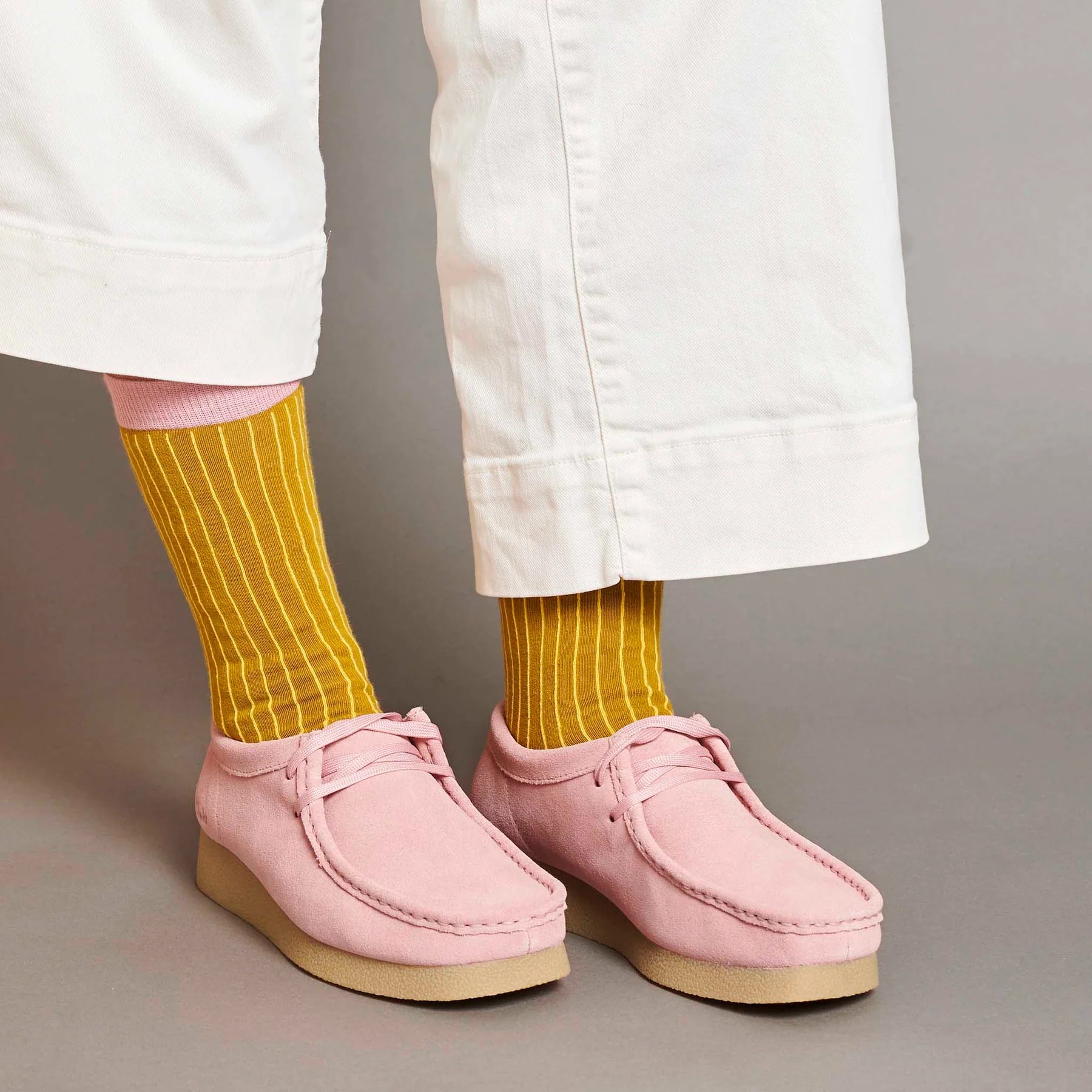 Person wearing pink shoes and yellow socks on a neutral background