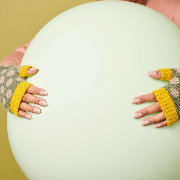 Large pale green balloon held gently by hands in speckled grey and yellow fingerless gloves.