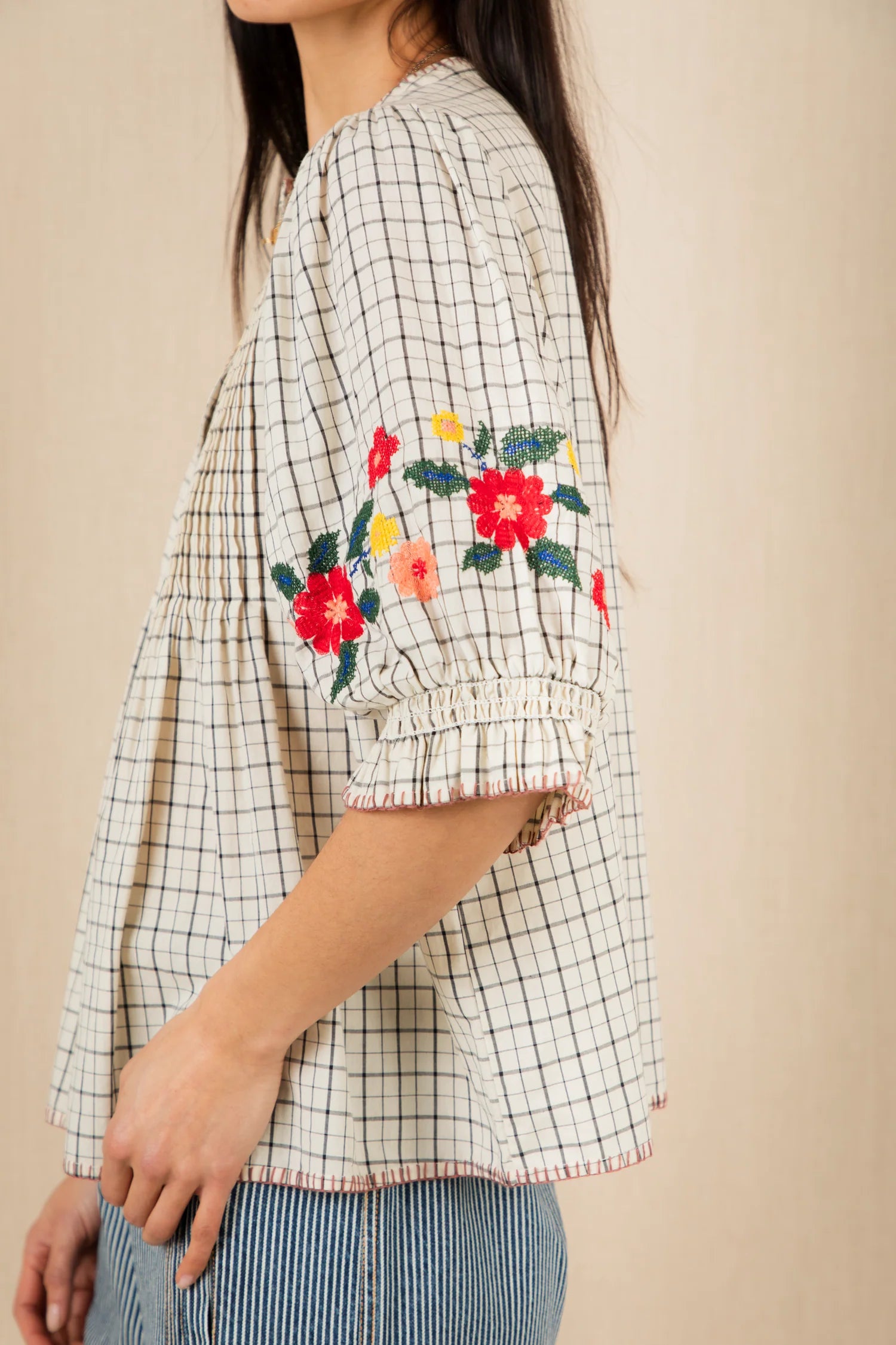 Woman wearing a checkered blouse with floral embroidery on a beige background