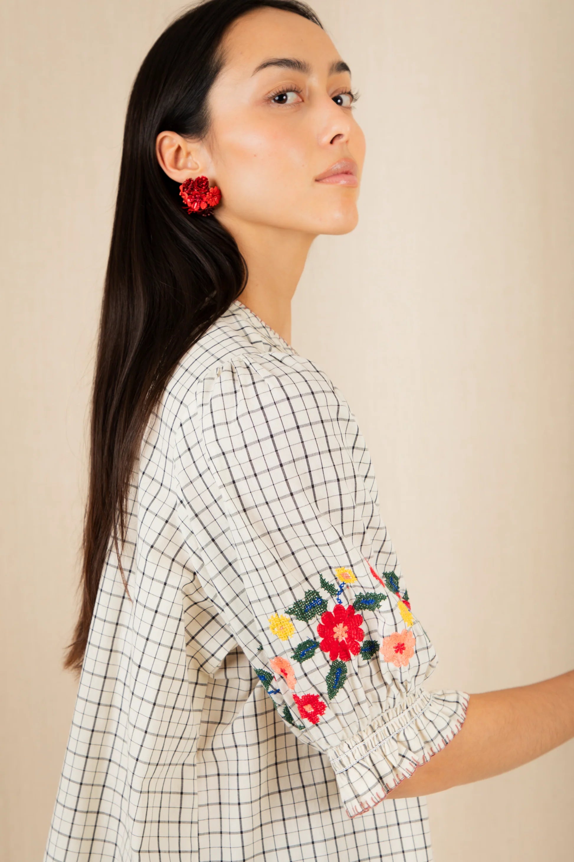 Woman wearing a checkered shirt with floral embroidery on a beige background